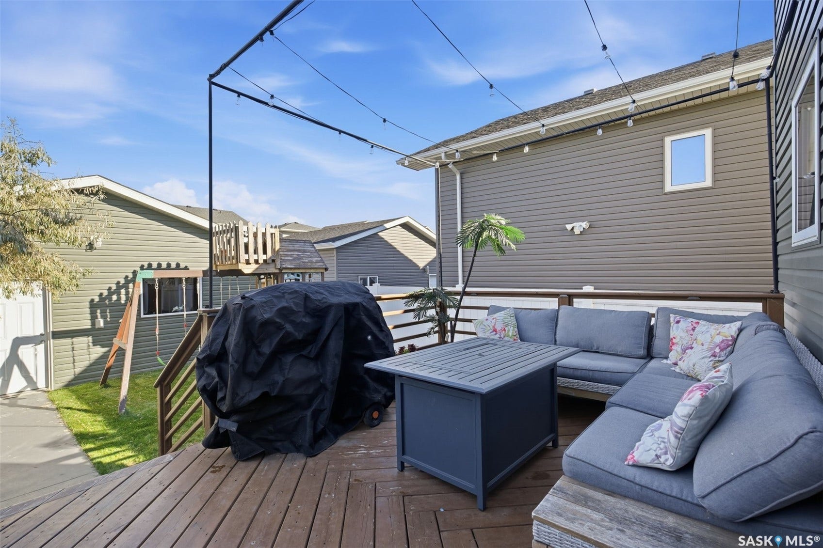 Spacious wood-finish deck with string lighting, brown railings, and gray siding exterior