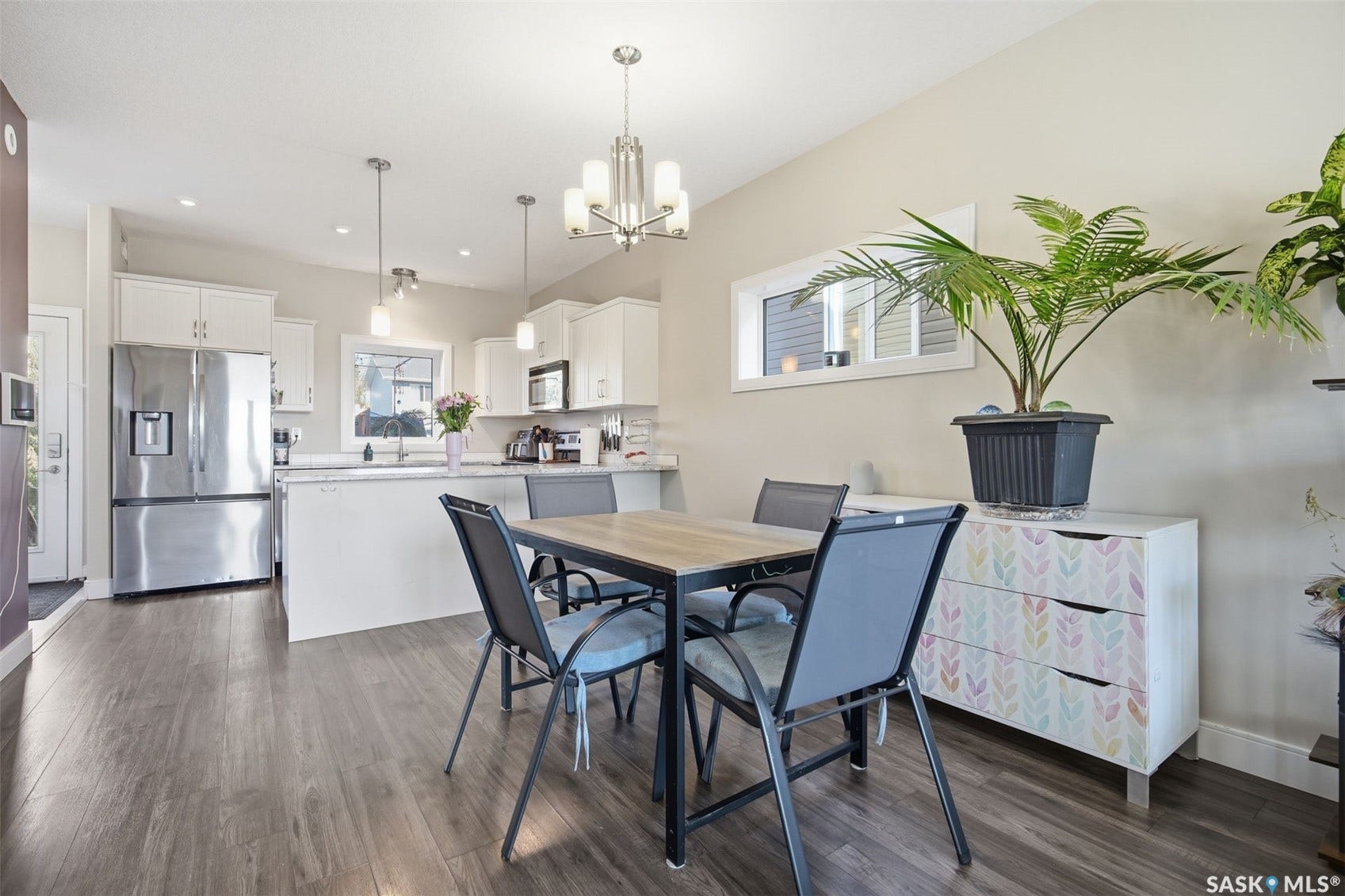 Open-concept kitchen and dining area featuring wood-finish flooring, white cabinetry, stainless steel appliances, and a kitchen island with seating
