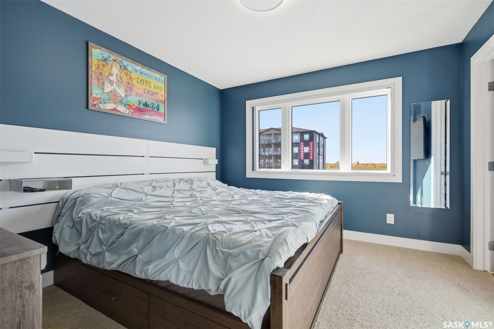 Carpeted bedroom featuring a large window, a ceiling-mounted light fixture, and a built-in headboard with integrated shelving