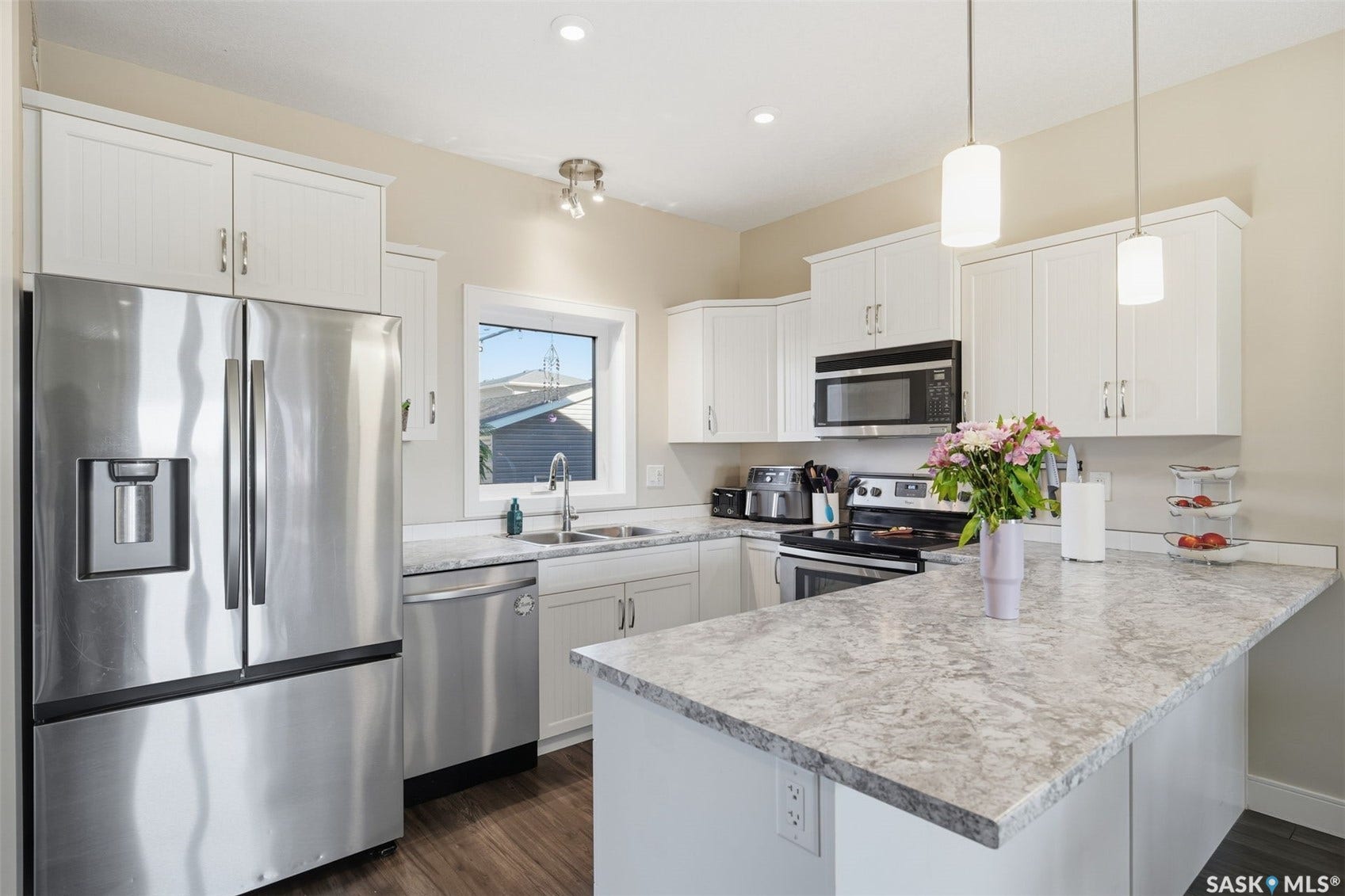 Modern kitchen featuring white cabinetry, stainless steel appliances, light-toned countertops, and wood-finish flooring