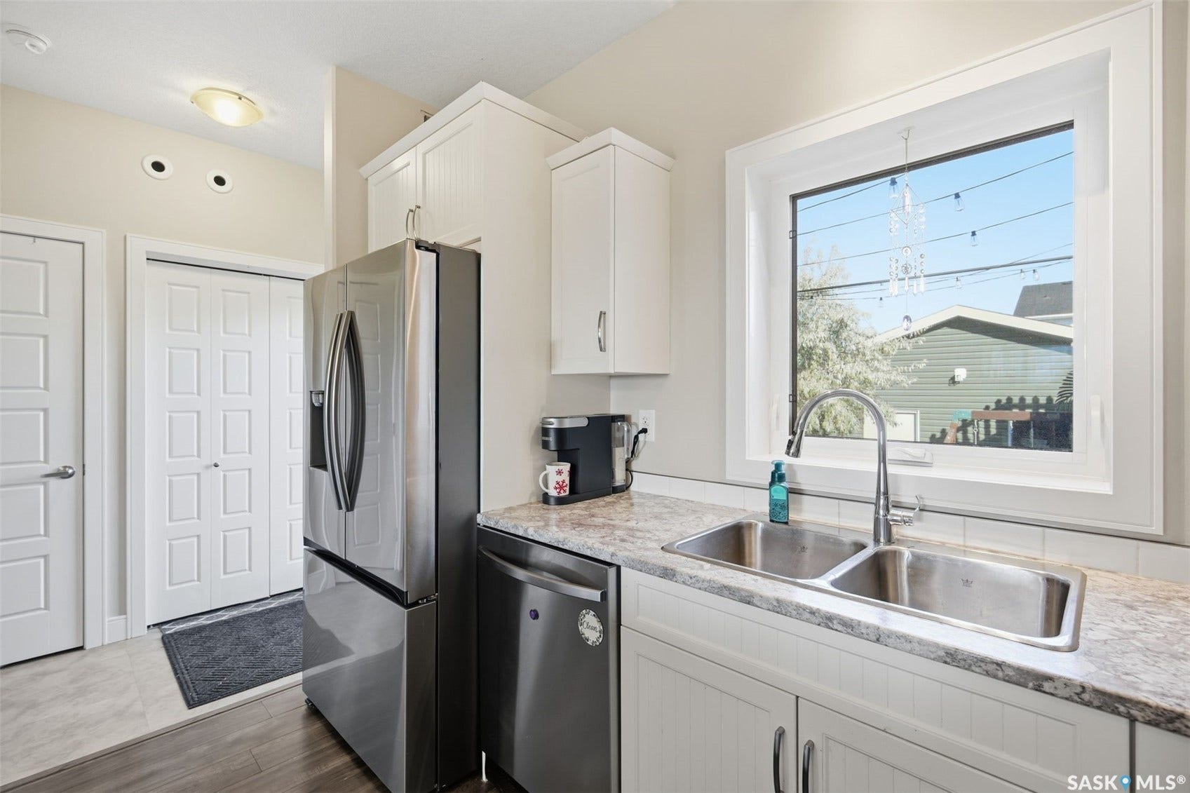 Stainless steel refrigerator and dishwasher, dual basin undermount sink, white shaker cabinetry, and light-toned countertop
