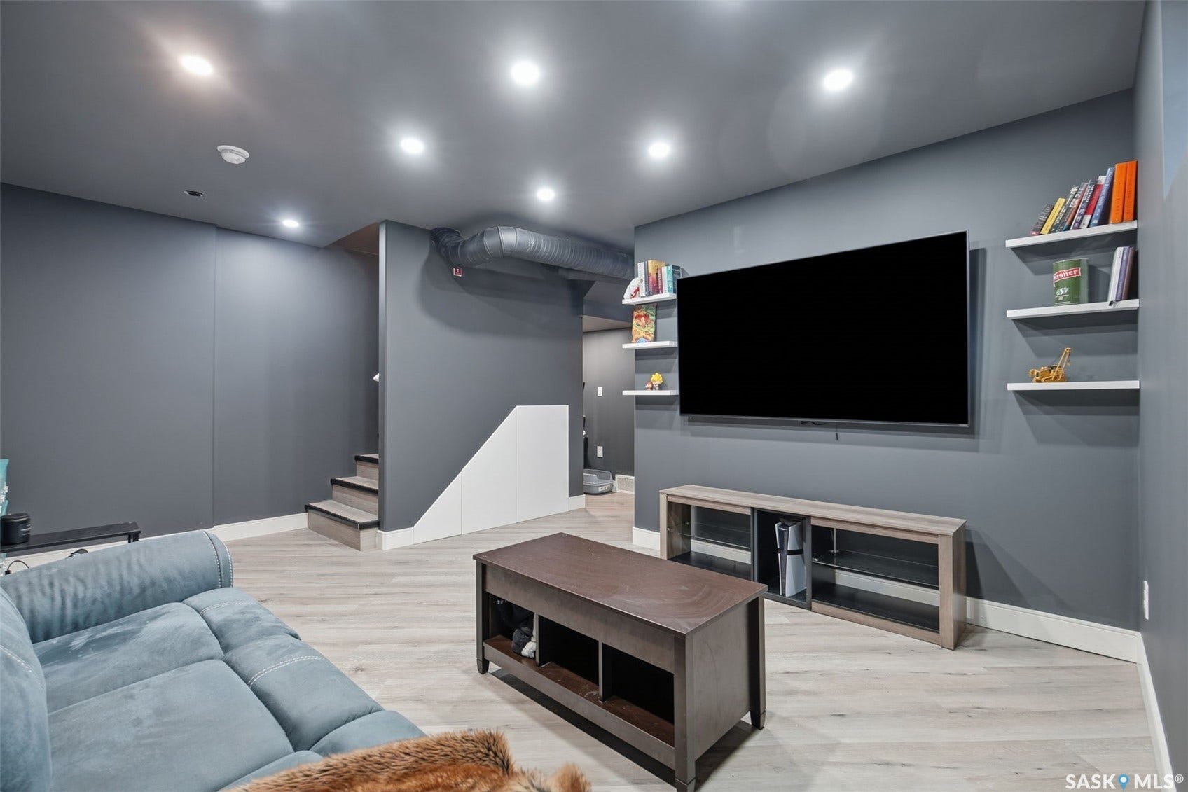Recessed lighting illuminates the space, featuring light wood-finish flooring and a staircase with a white half-wall