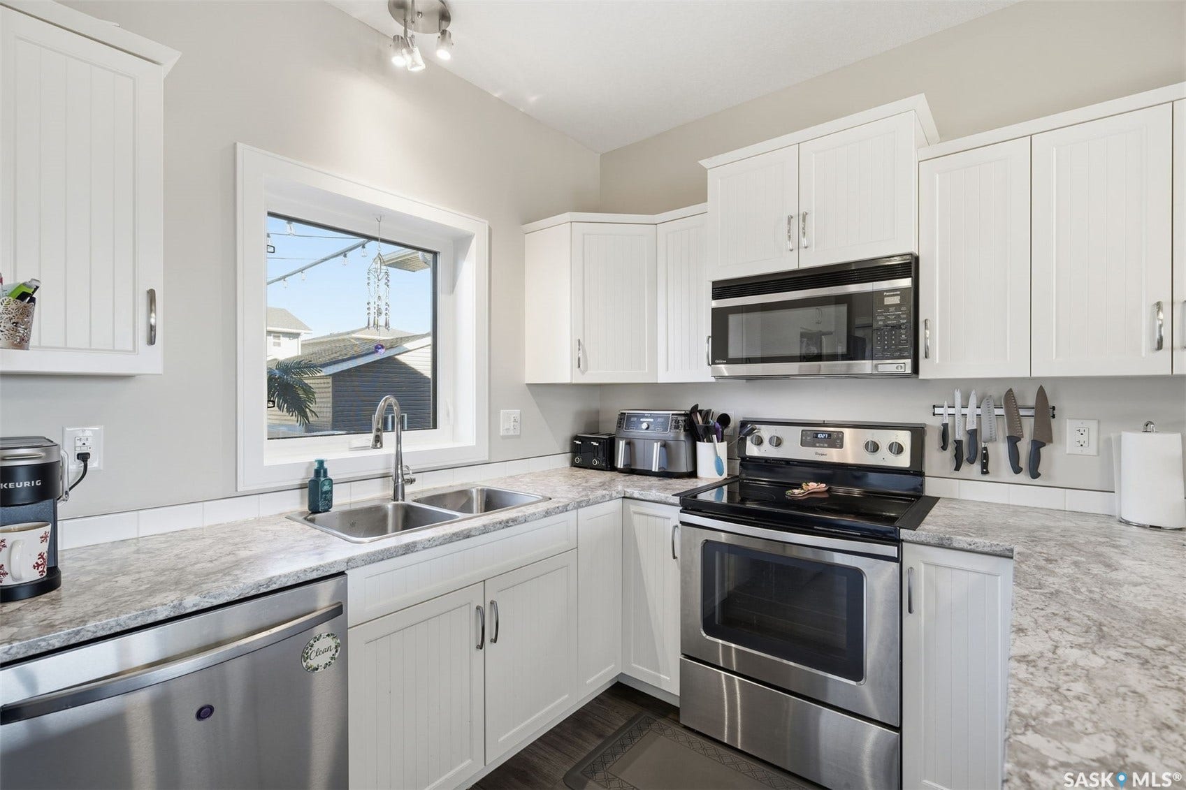 Modern kitchen with white cabinetry, stainless steel appliances, a dual basin sink, and wood-finish flooring