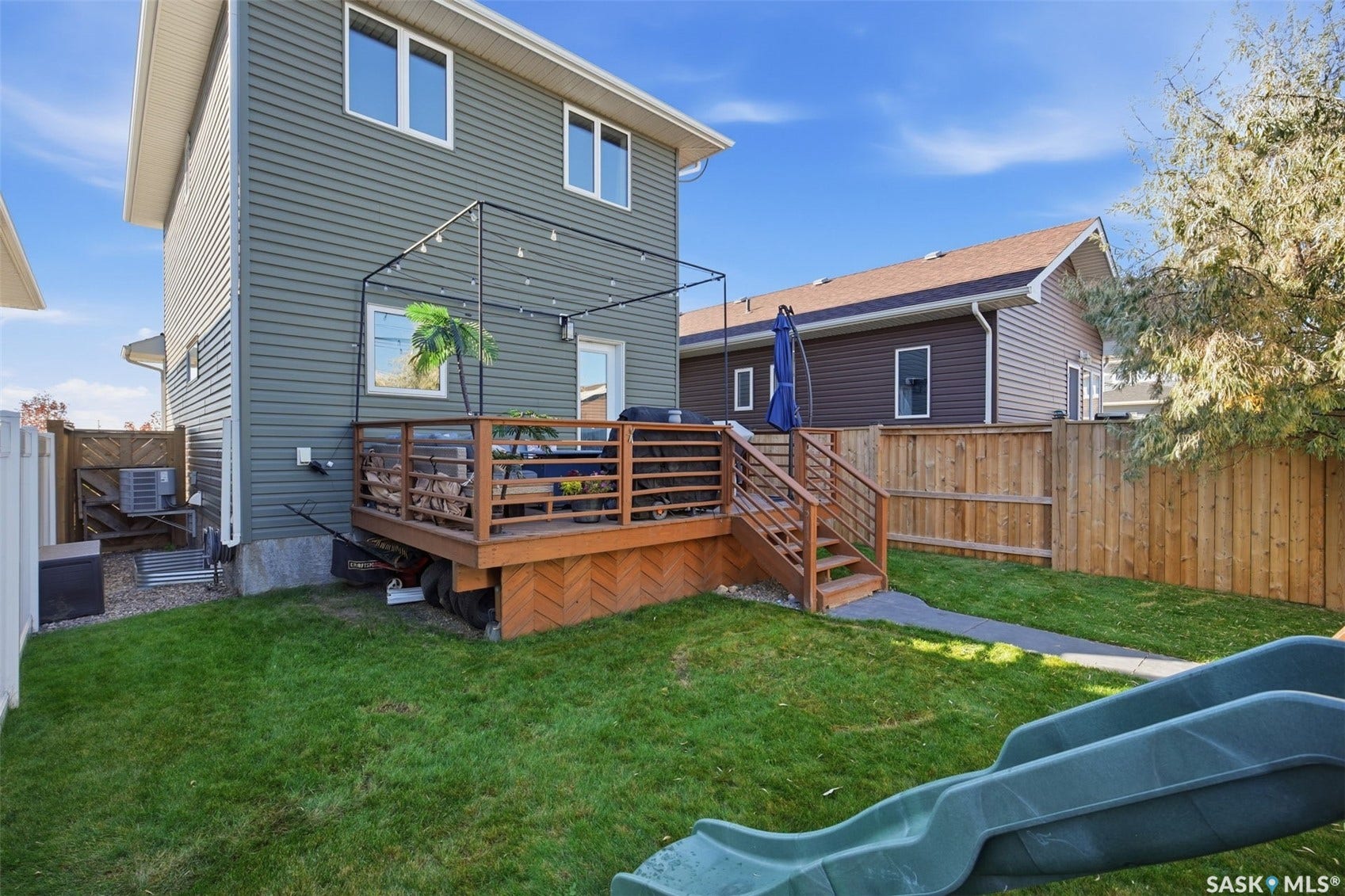 Exterior featuring dark gray siding, a wood-finish deck with metal railings, a pergola structure, and a fenced backyard with a grass lawn