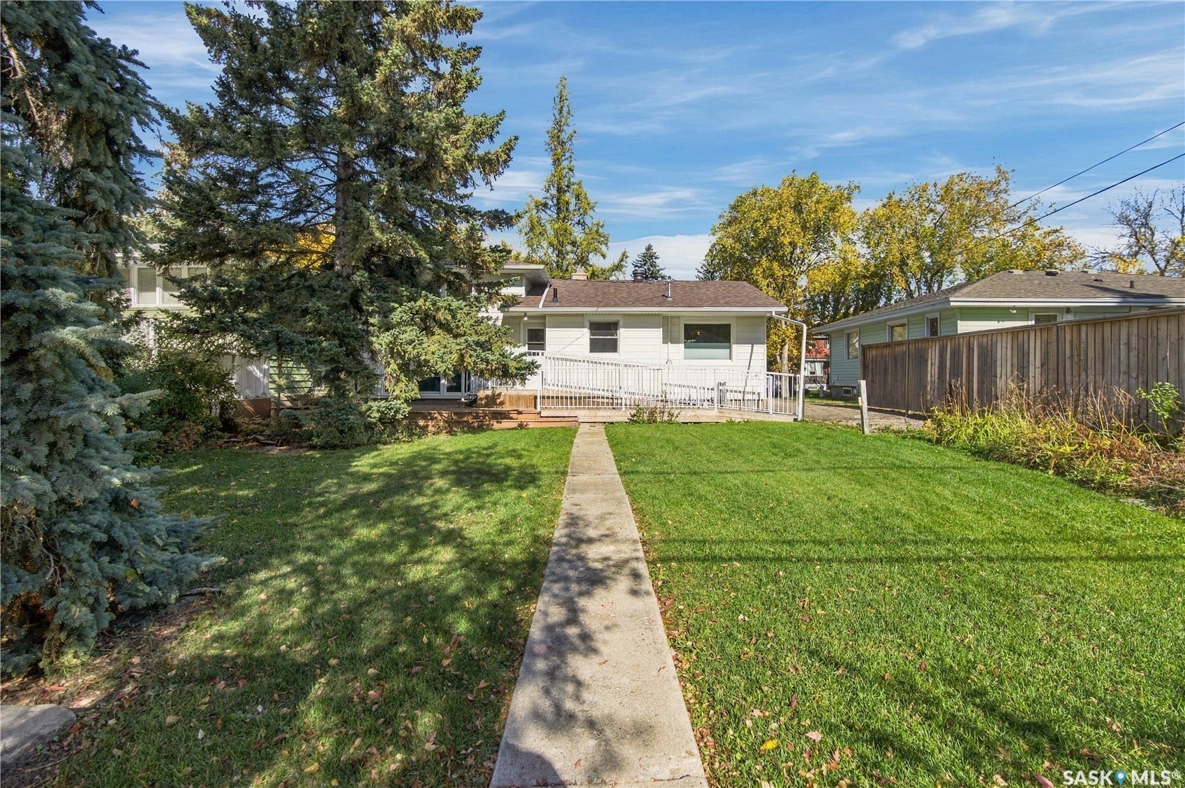 2727 Assiniboine Avenue, Regina SK S4S 1C7 Expansive green lawn with mature evergreen trees and a concrete pathway leading to the rear of the property