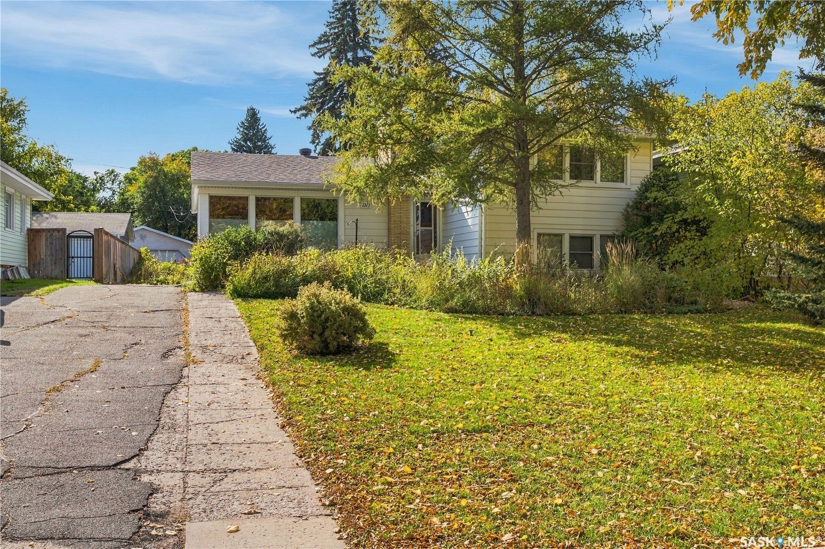 2727 Assiniboine Avenue, Regina SK S4S 1C7 White siding exterior with multiple windows, surrounded by mature trees and established landscaping