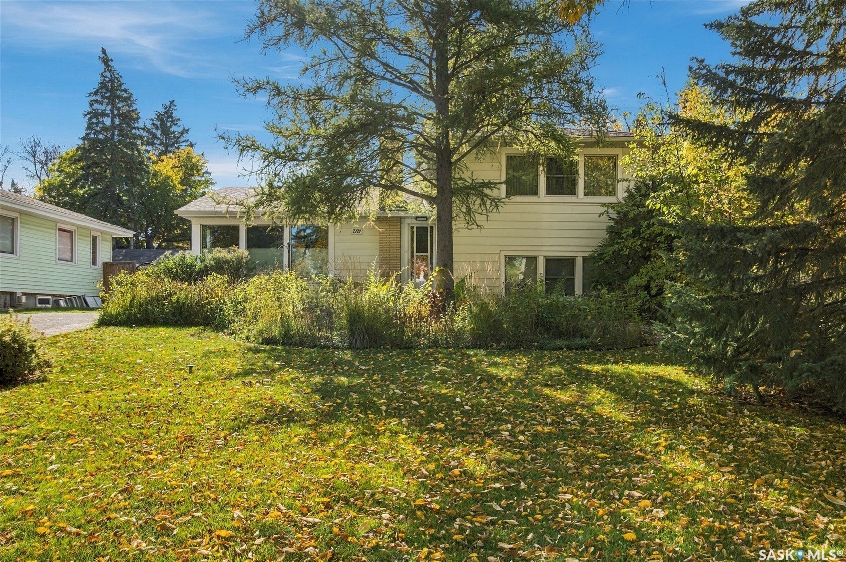 2727 Assiniboine Avenue, Regina SK S4S 1C7 Two-story siding exterior with multiple windows, surrounded by mature trees and established landscaping