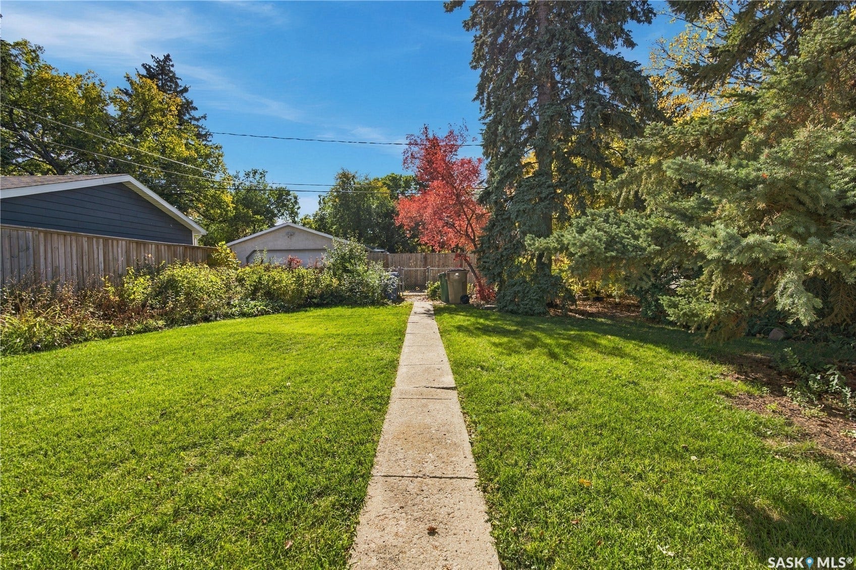 2727 Assiniboine Avenue, Regina SK S4S 1C7 Expansive lawn area with a concrete walkway, mature trees, and a wooden fence