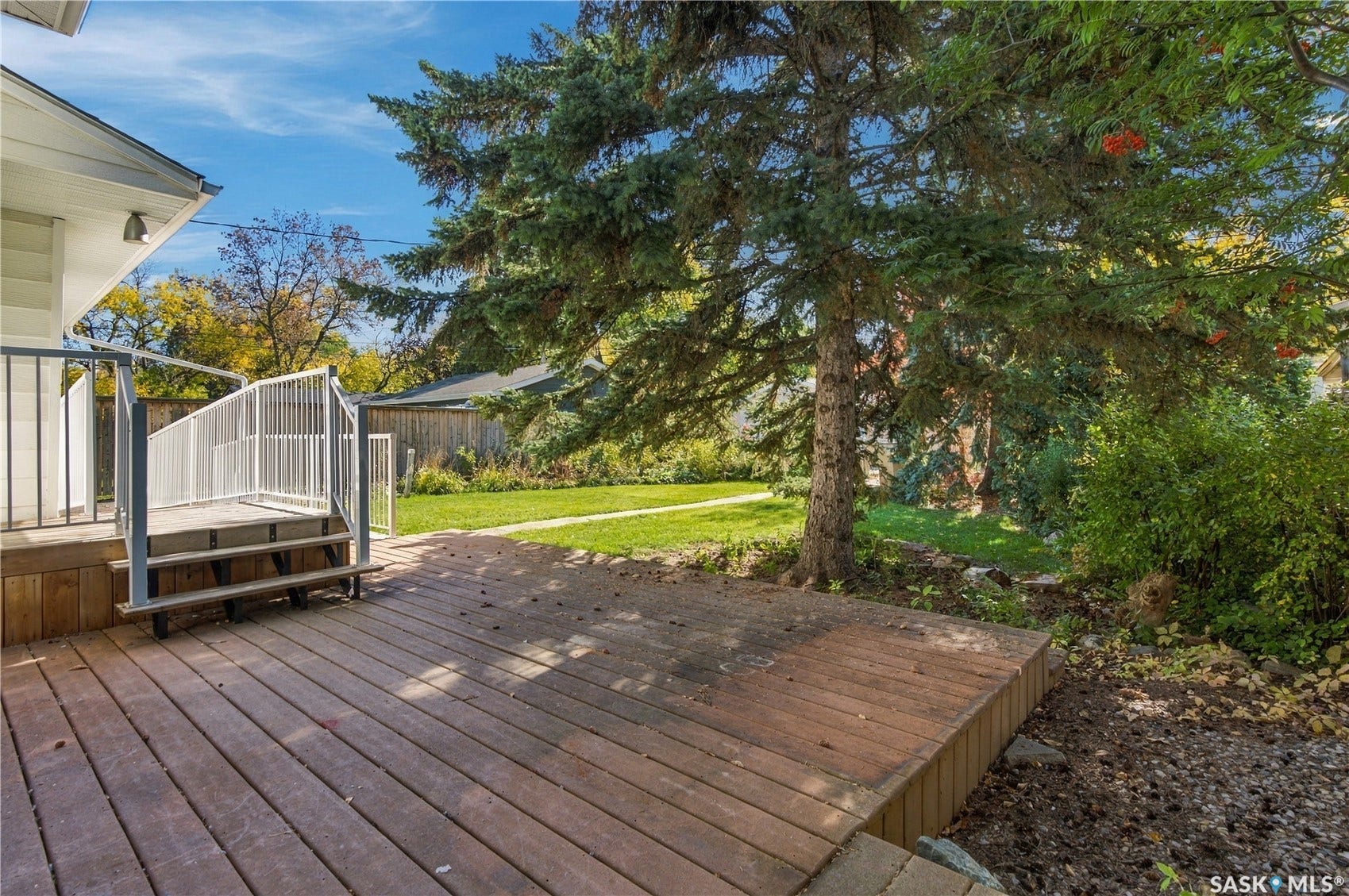 2727 Assiniboine Avenue, Regina SK S4S 1C7 Wood-finish deck with white metal railings, integrated steps, and mature tree landscaping