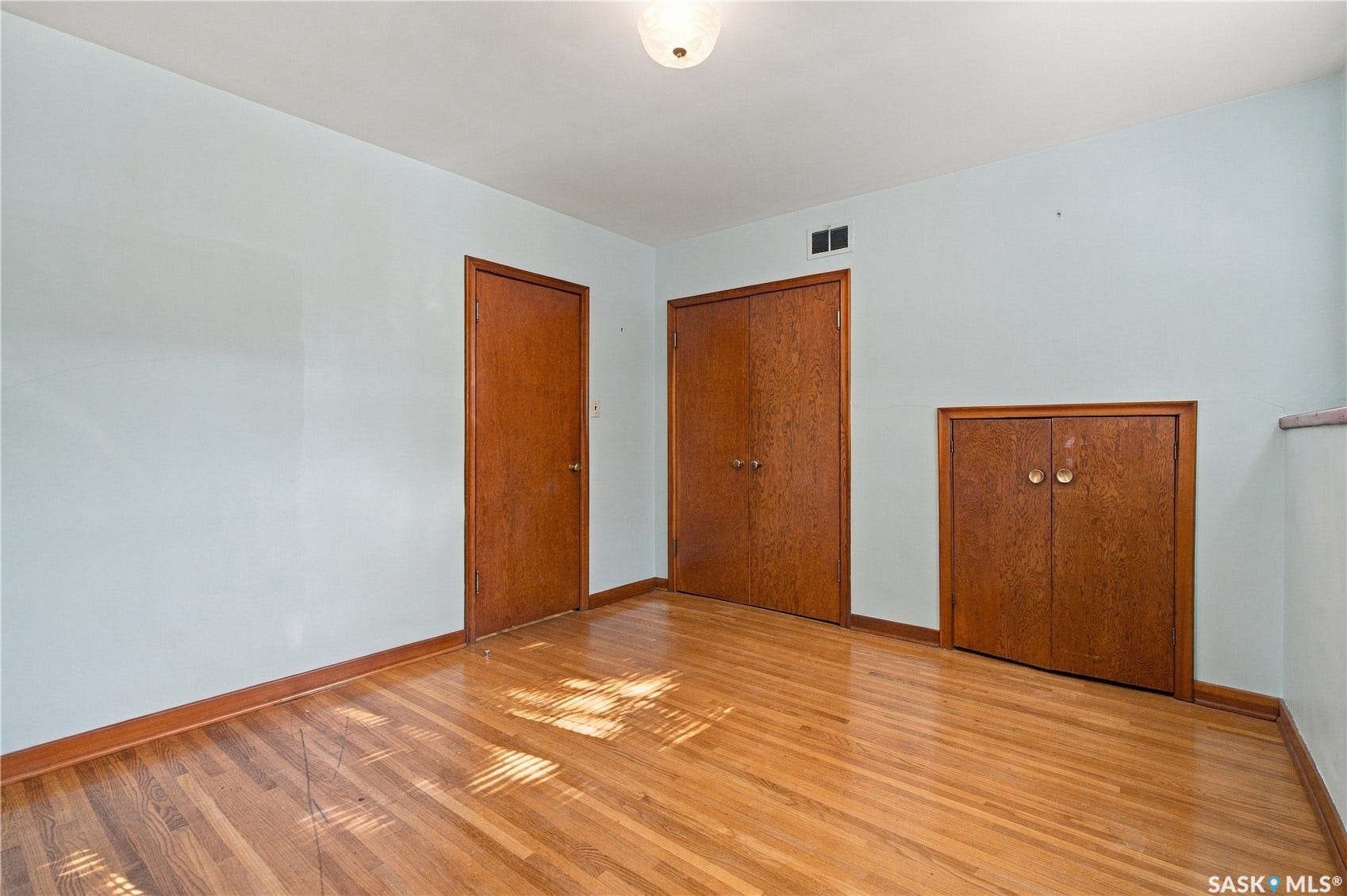 2727 Assiniboine Avenue, Regina SK S4S 1C7 Hardwood flooring, light blue wall paint, wood-finish doors, and built-in wood-finish cabinetry