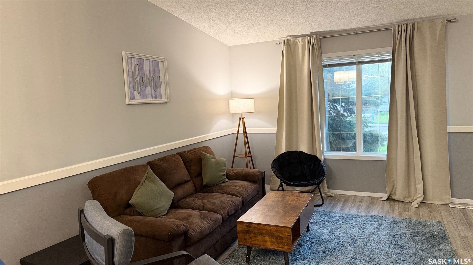 Two-tone wall treatment with chair rail, window with installed curtain rod, and wood-finish flooring