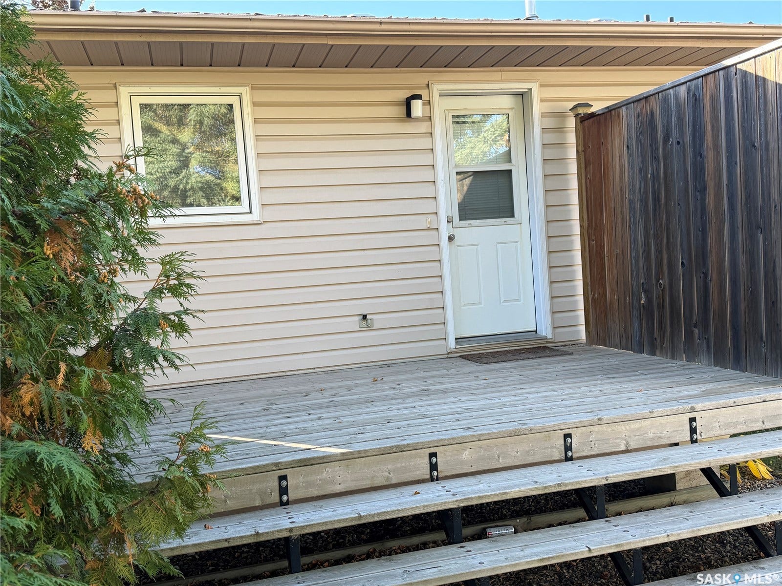Raised wood deck with built-in steps, light-colored vinyl siding, and a white exterior door
