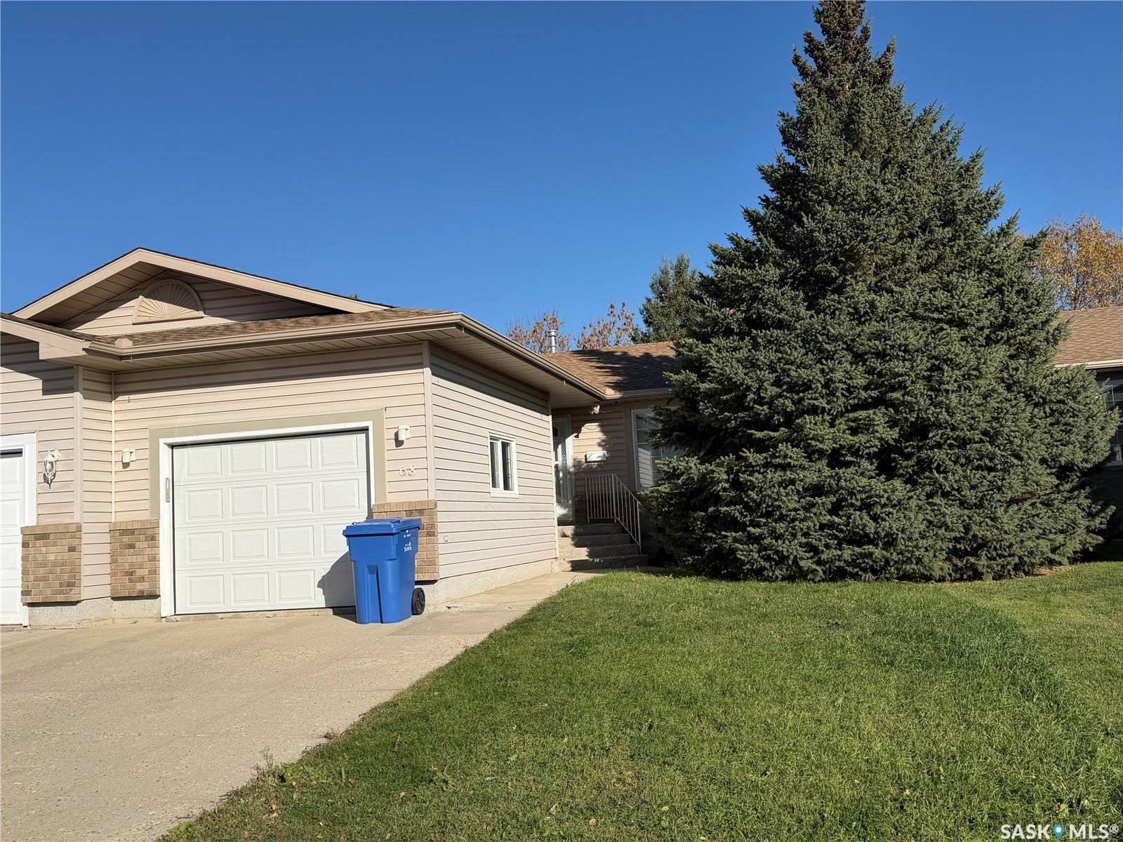 Siding exterior with brick accents, attached garage, sloped roofing, mature front yard tree, and front lawn