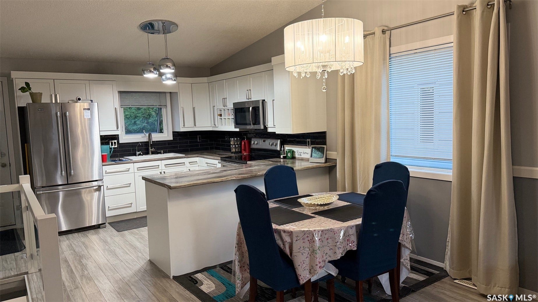 Kitchen featuring white cabinetry, stainless steel appliances, dark subway tile backsplash, a center island with a stone-finish countertop, and wood-finish flooring