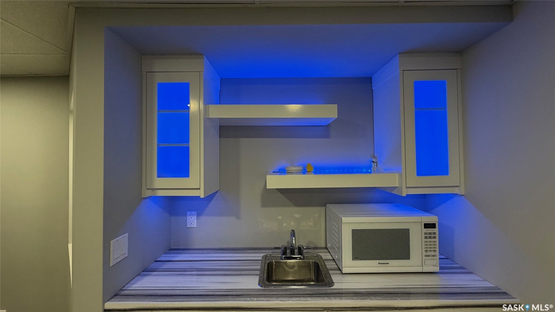 Built-in wet bar featuring a stainless steel sink, wood-finish countertop, and white cabinetry with accent lighting