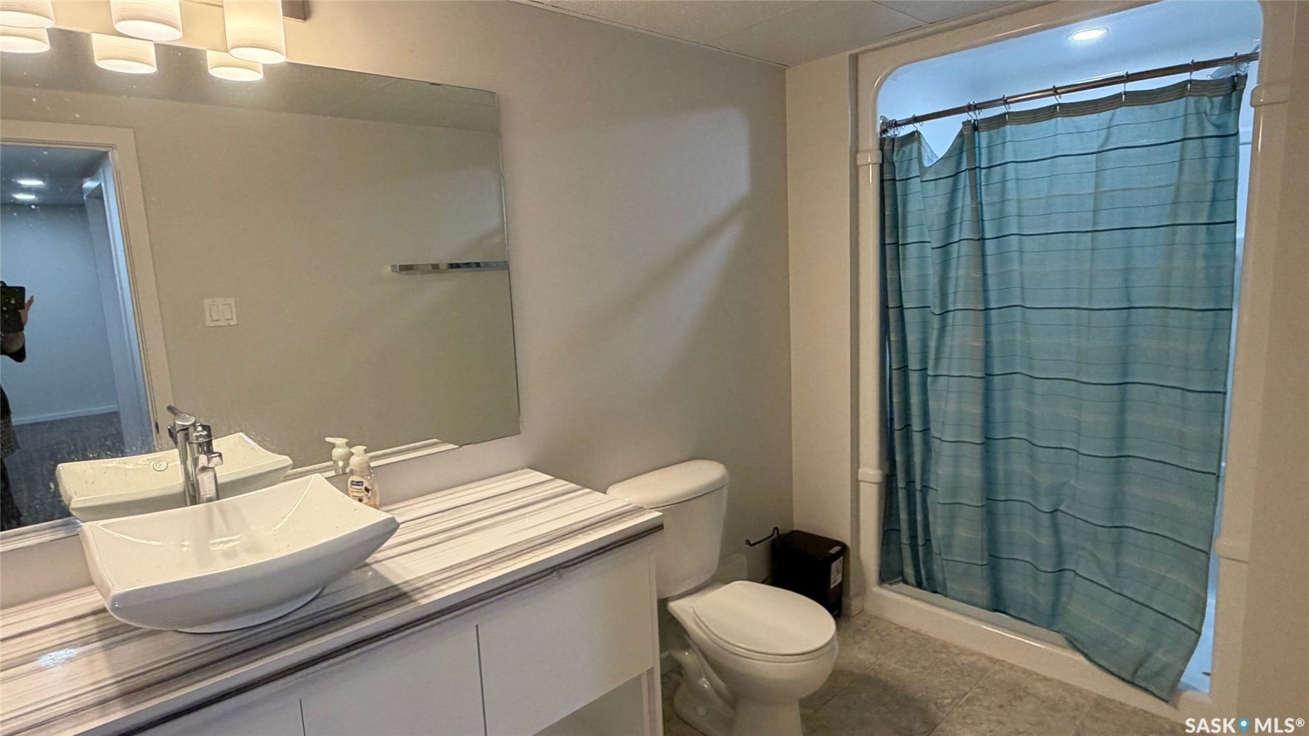 Bathroom featuring a vessel sink, vanity with a striped countertop, chrome faucet, and a shower with a tiled surround