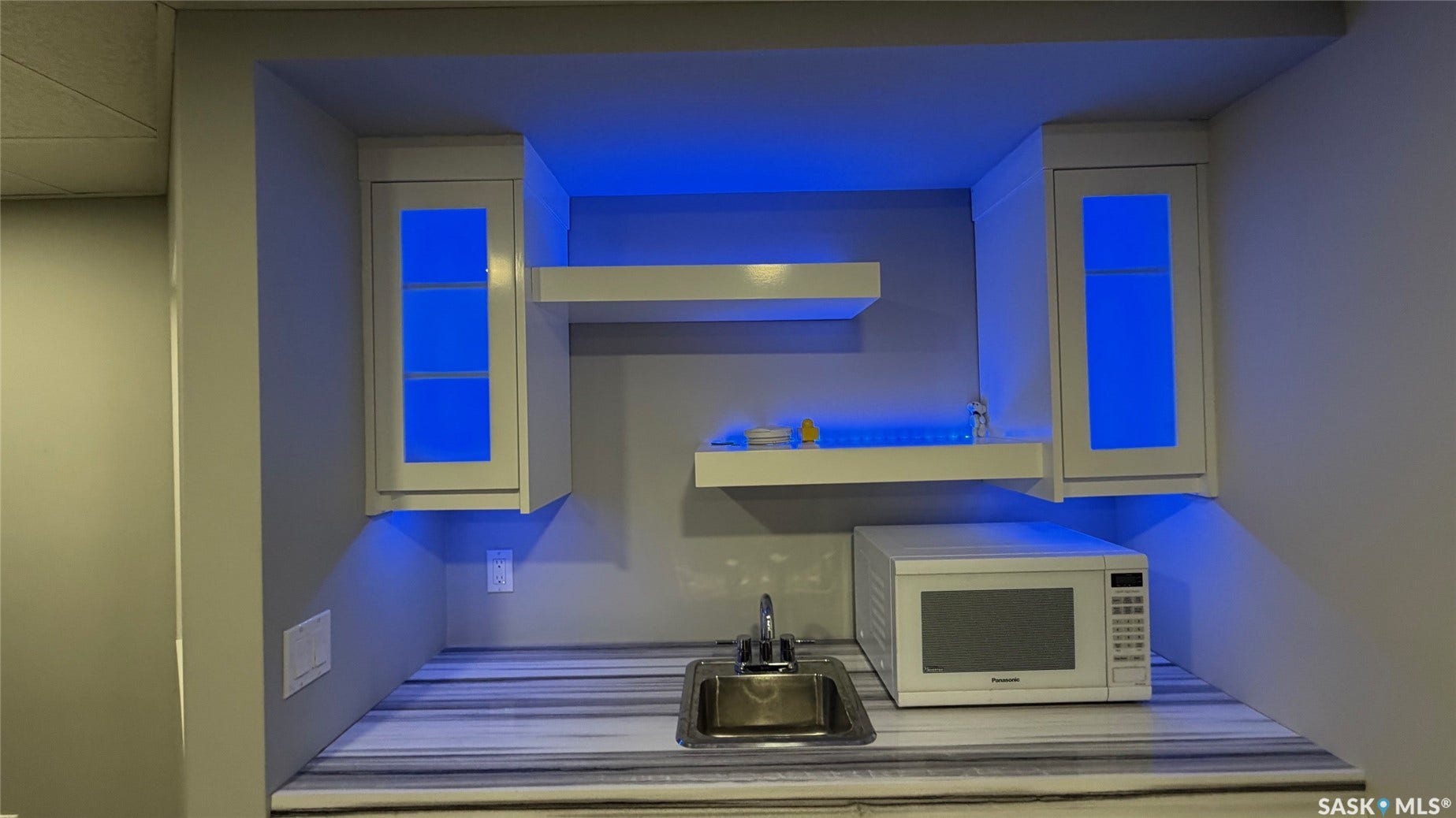 Built-in cabinetry with glass panel doors, floating shelves, stainless steel sink, and patterned countertop