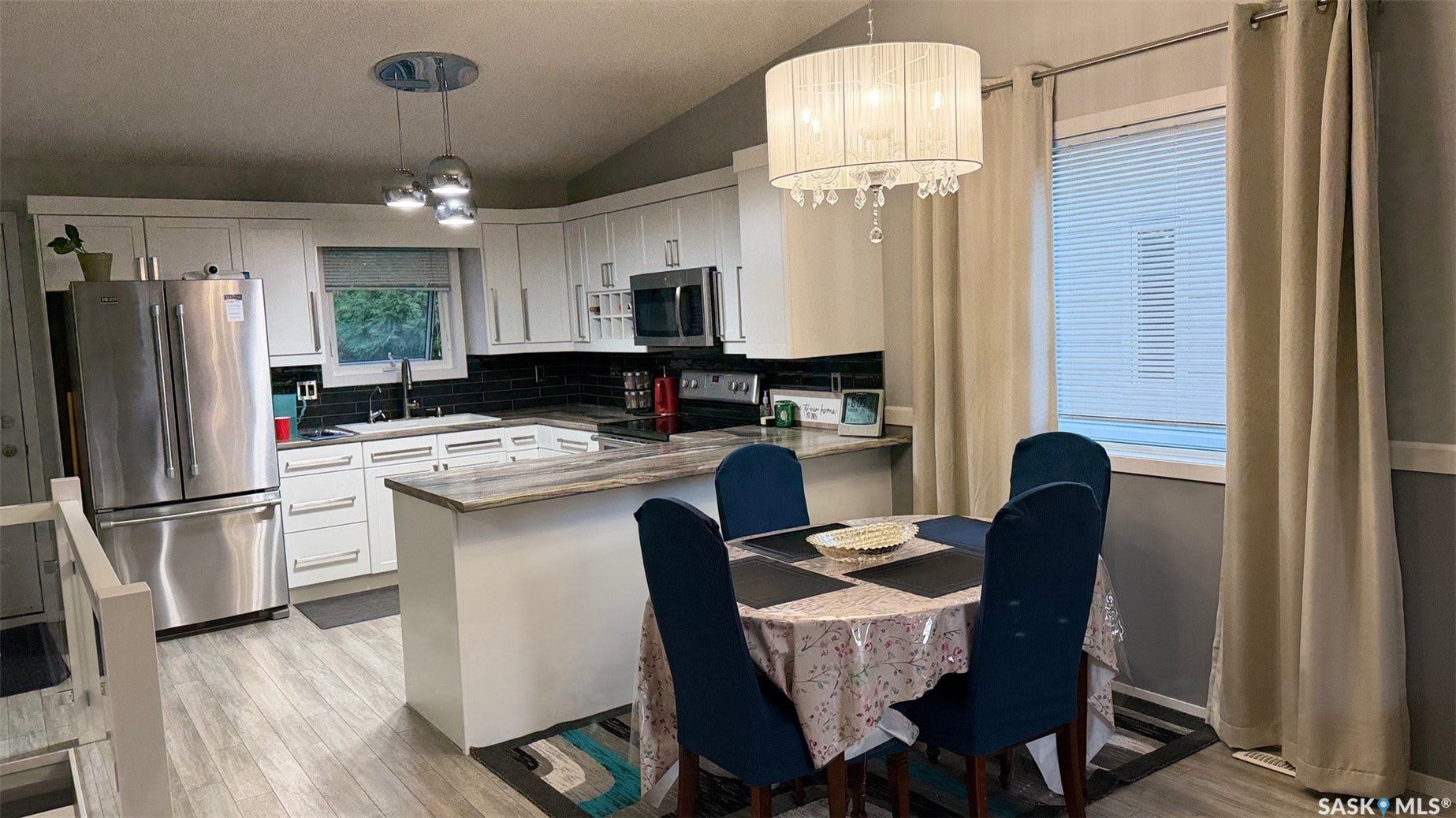 Kitchen featuring white cabinetry, stainless steel appliances, dark subway tile backsplash, and light wood-finish flooring
