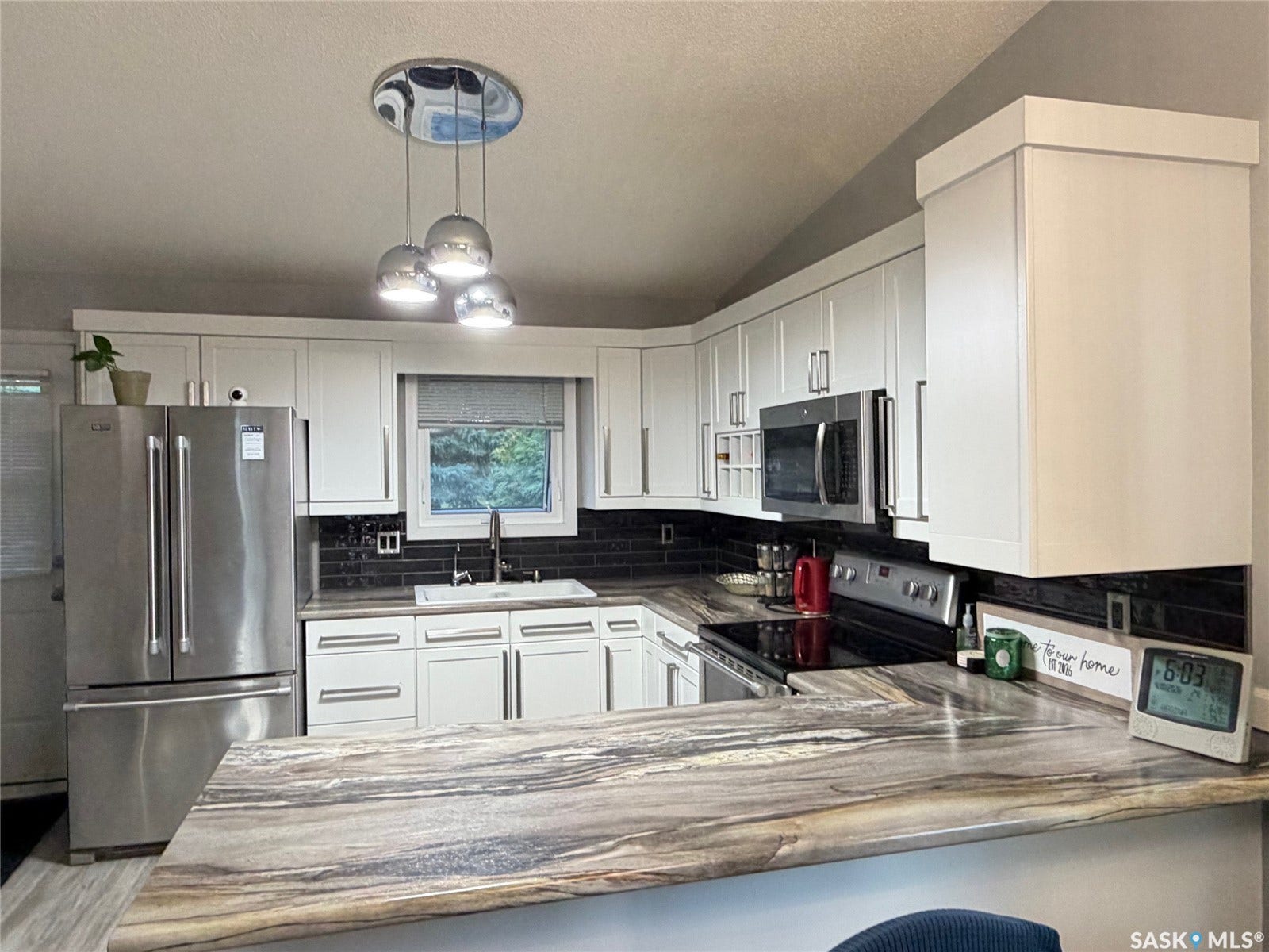 Kitchen featuring white cabinetry, stainless steel appliances, a dark subway tile backsplash, a white undermount sink, and a multi-tone countertop