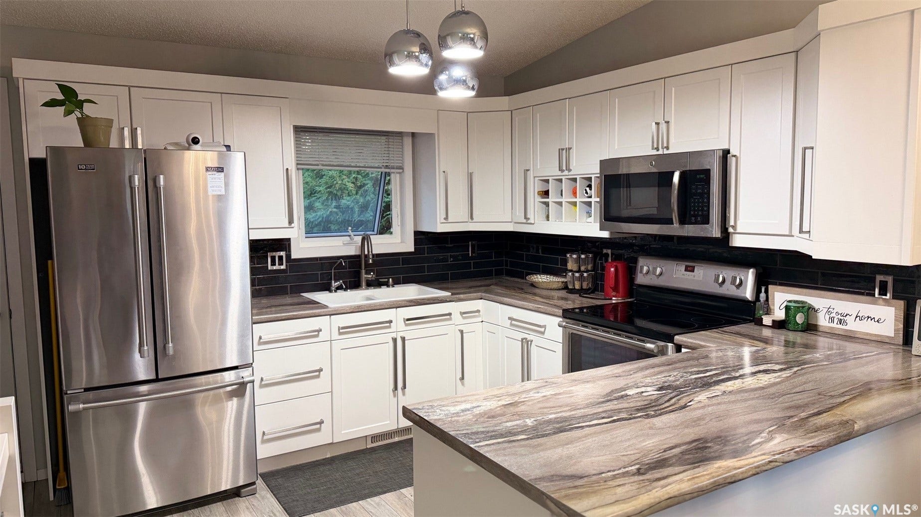 White shaker-style cabinetry, dark subway tile backsplash, stainless steel appliances, modern pendant lighting, and a patterned countertop