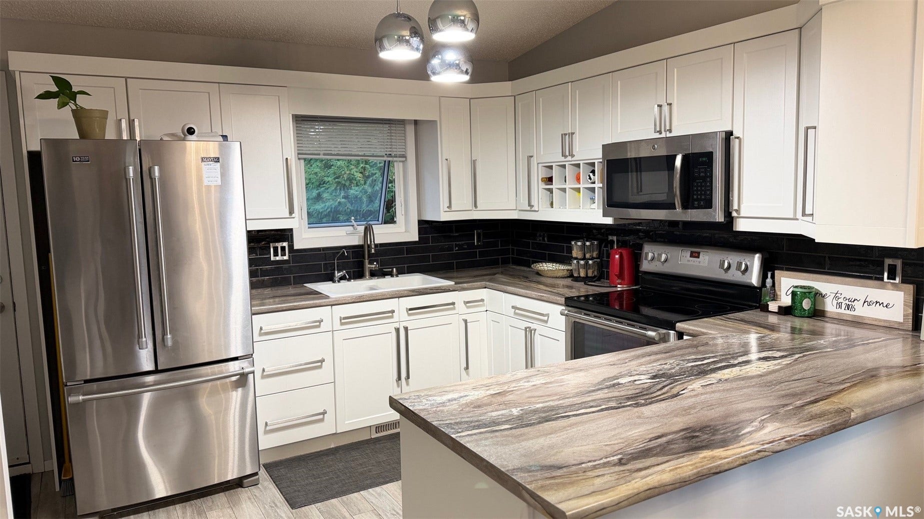 Kitchen featuring white cabinetry, a black subway tile backsplash, stainless steel appliances, and patterned countertops