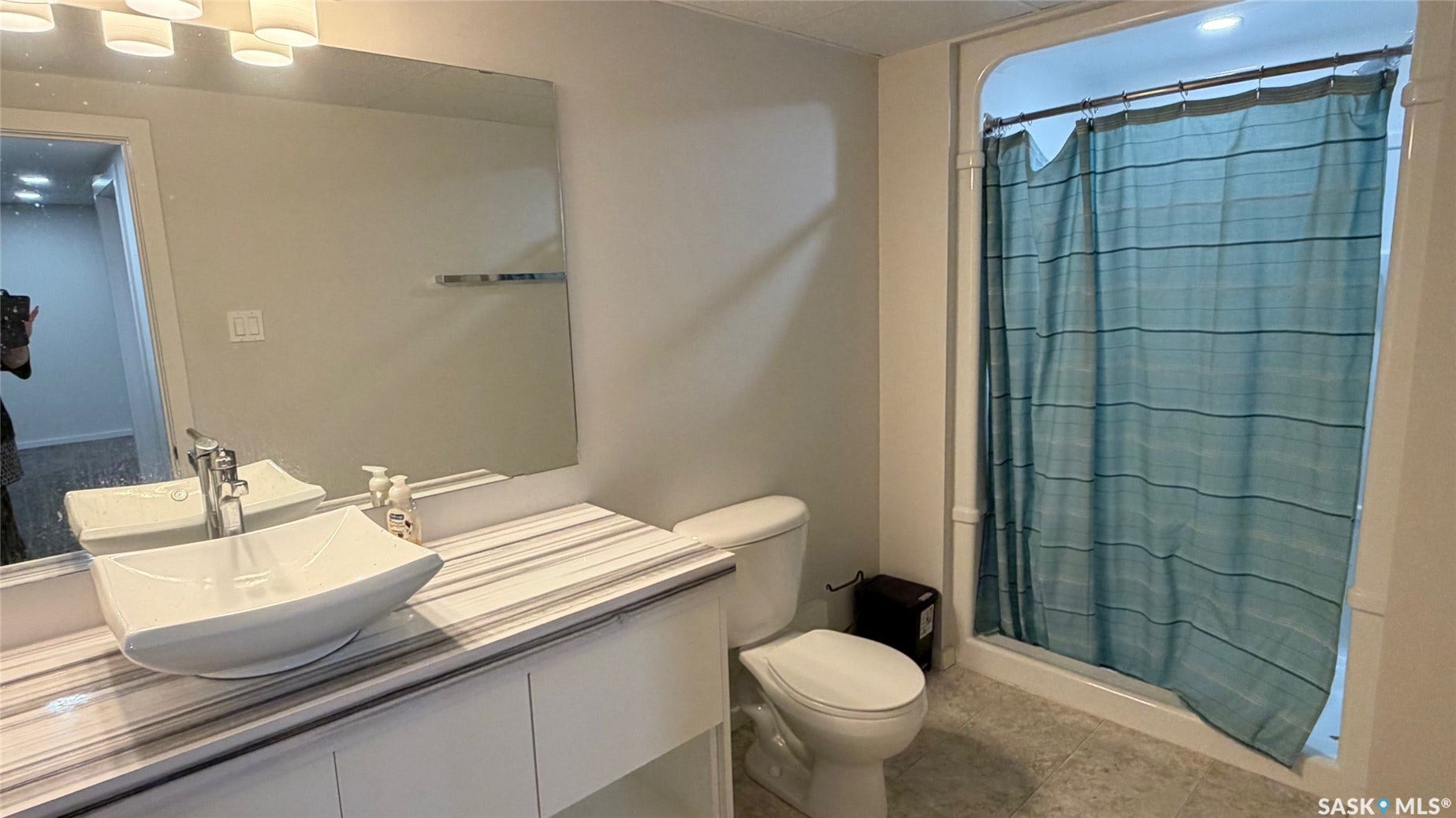 Vanity with vessel sink, wall-mounted mirror, overhead lighting, toilet, and shower enclosure