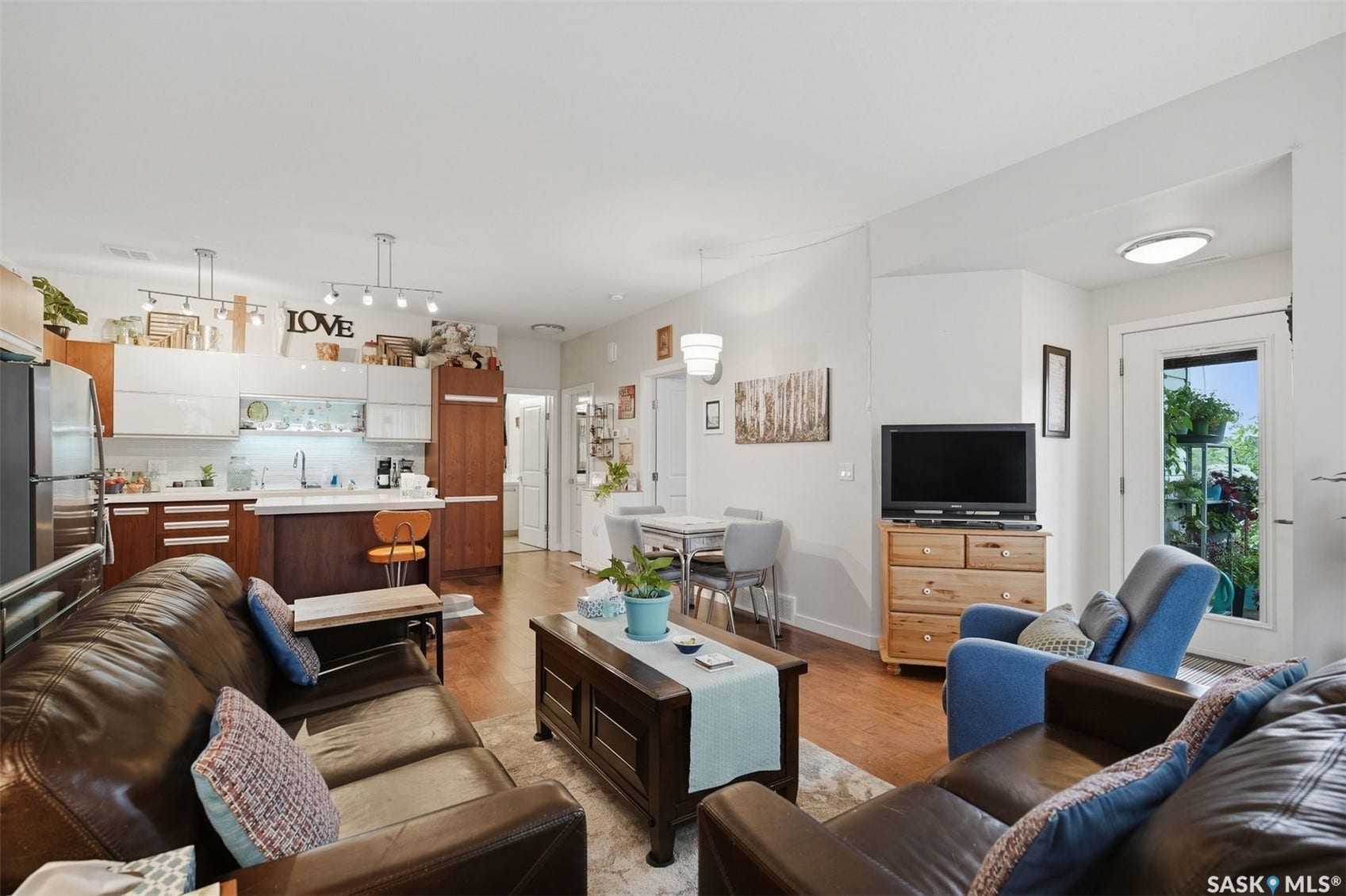 Open-concept living area featuring wood-finish flooring, white walls, kitchen with white upper and wood lower cabinetry, and a dining area with pendant lighting