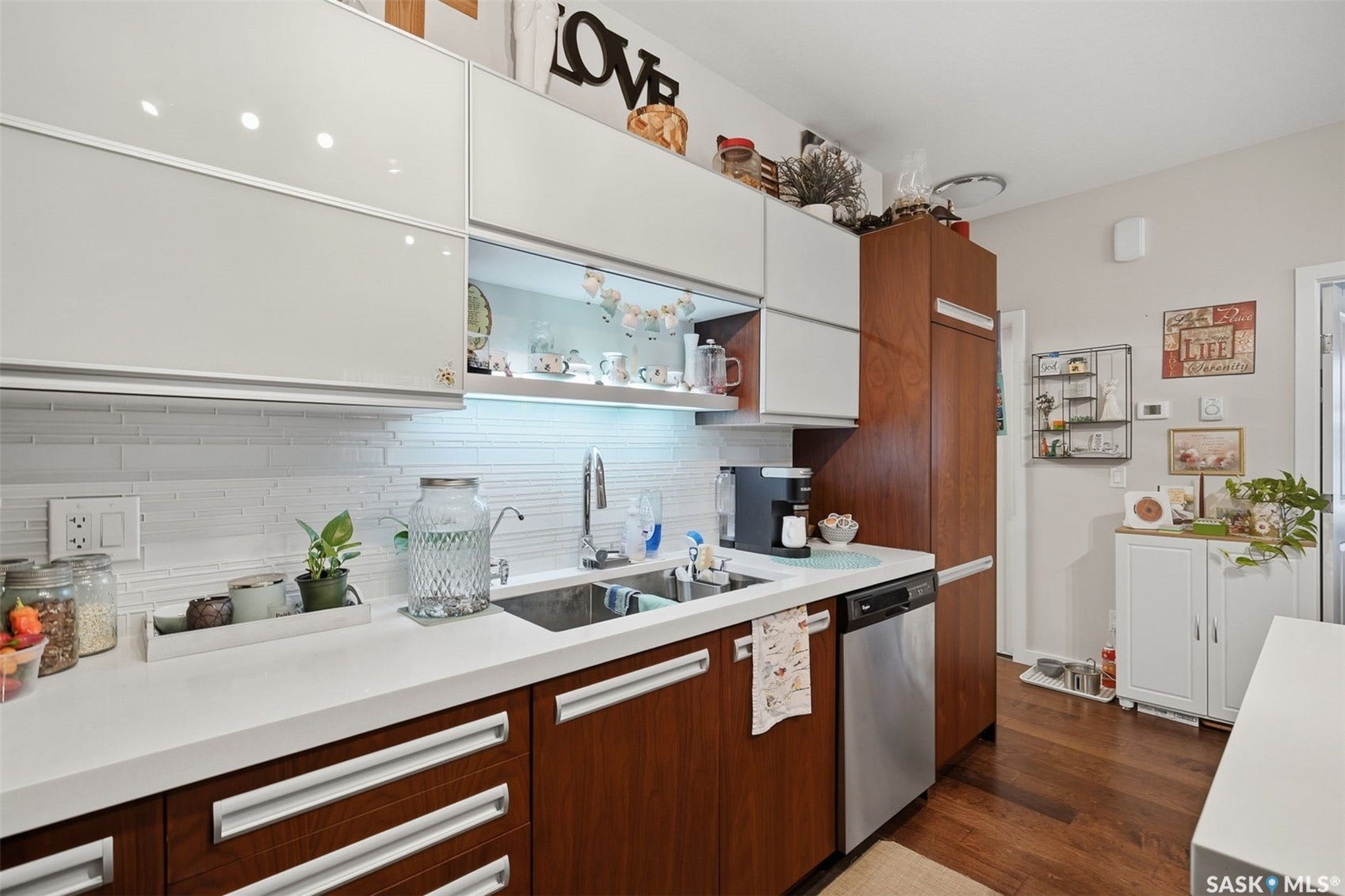 Kitchen featuring white upper cabinetry, wood-finish lower cabinetry, a stainless steel dishwasher, a stainless steel sink, and wood-finish flooring