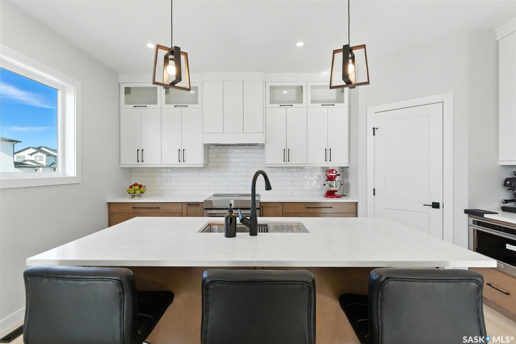Kitchen featuring a large island with sink, white shaker cabinetry, wood-finish base cabinets, subway tile backsplash, and contemporary pendant lighting