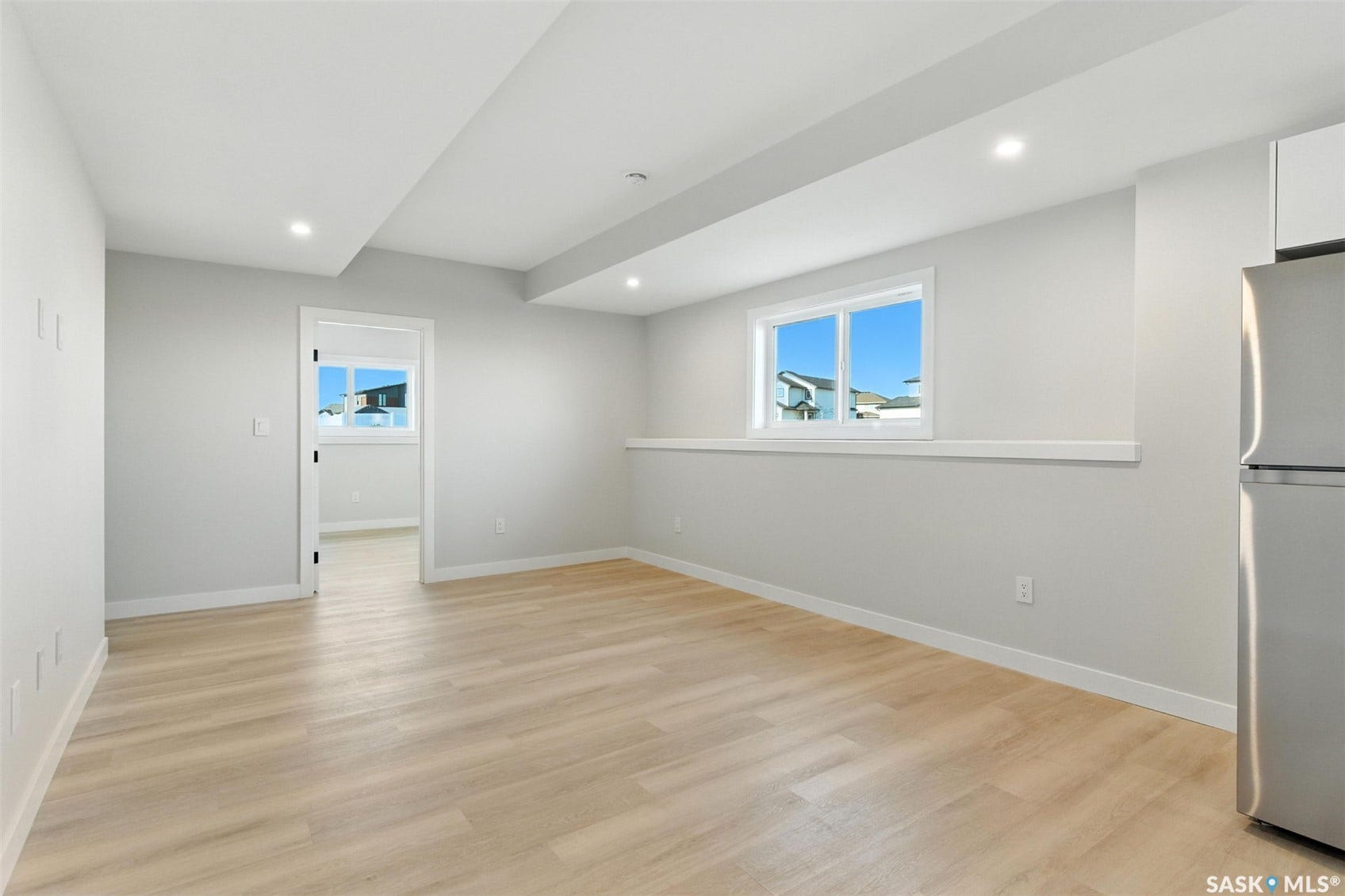 Recessed lighting, wood-finish flooring, white trim, and a stainless steel refrigerator