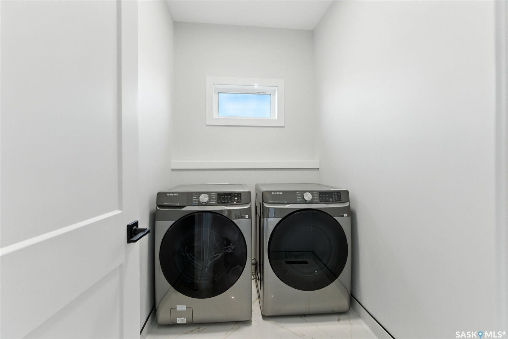 Laundry area featuring a compact window, white walls, and a light-toned flooring
