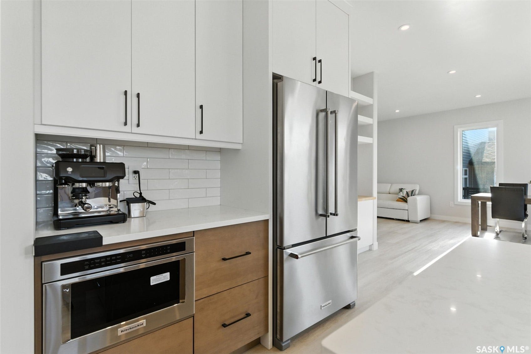 White shaker-style cabinetry with matte black hardware, subway tile backsplash, stainless steel appliances, wood-finish lower cabinetry, and recessed lighting