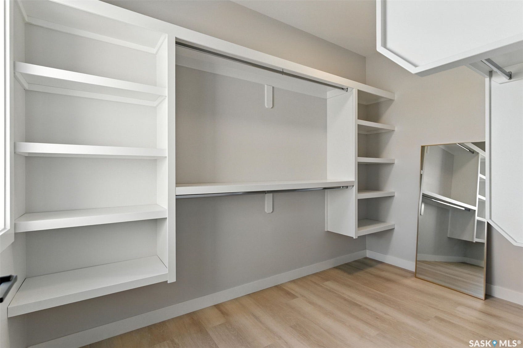 Built-in closet system featuring white shelving, hanging rods, and wood-finish flooring
