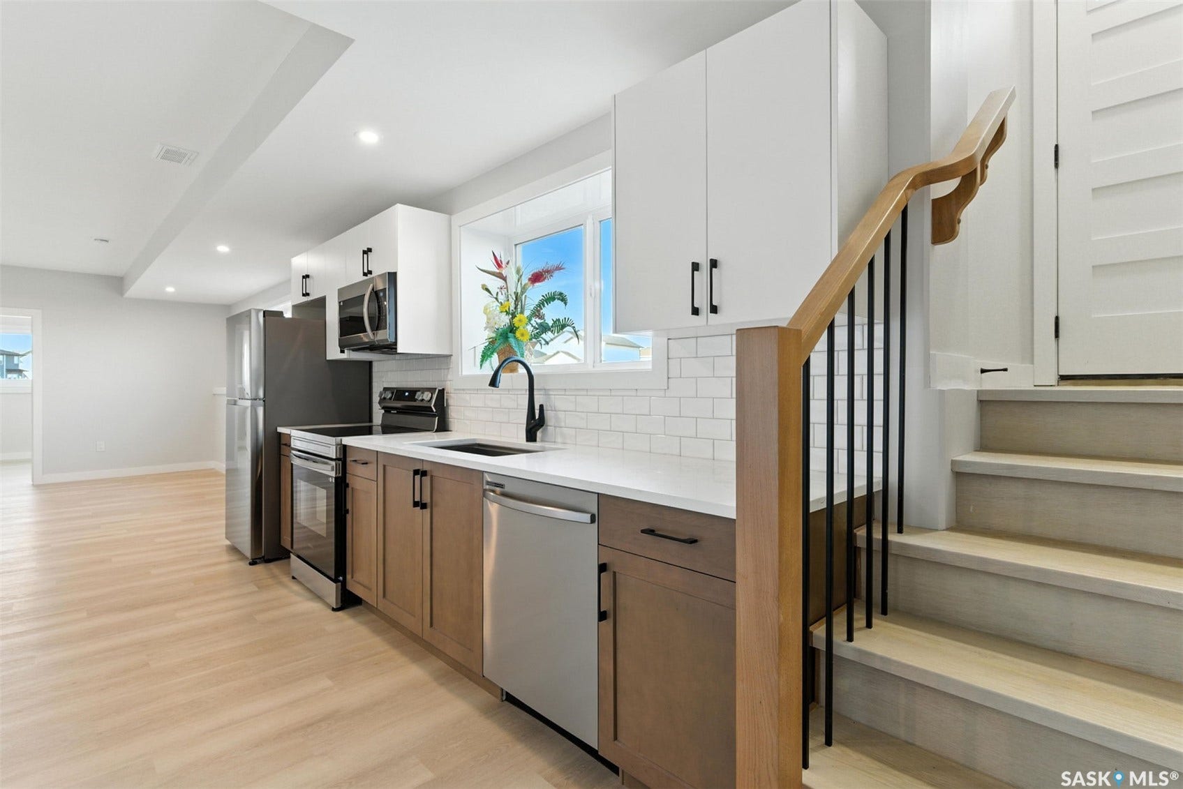 Modern kitchen with stainless steel appliances, white subway tile backsplash, light wood-finish flooring, and white upper cabinetry