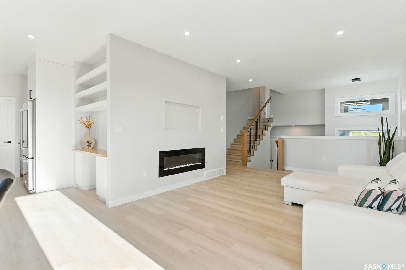 Light wood-finish flooring, recessed lighting, built-in shelving, integrated electric fireplace, and a light wood staircase with metal balusters