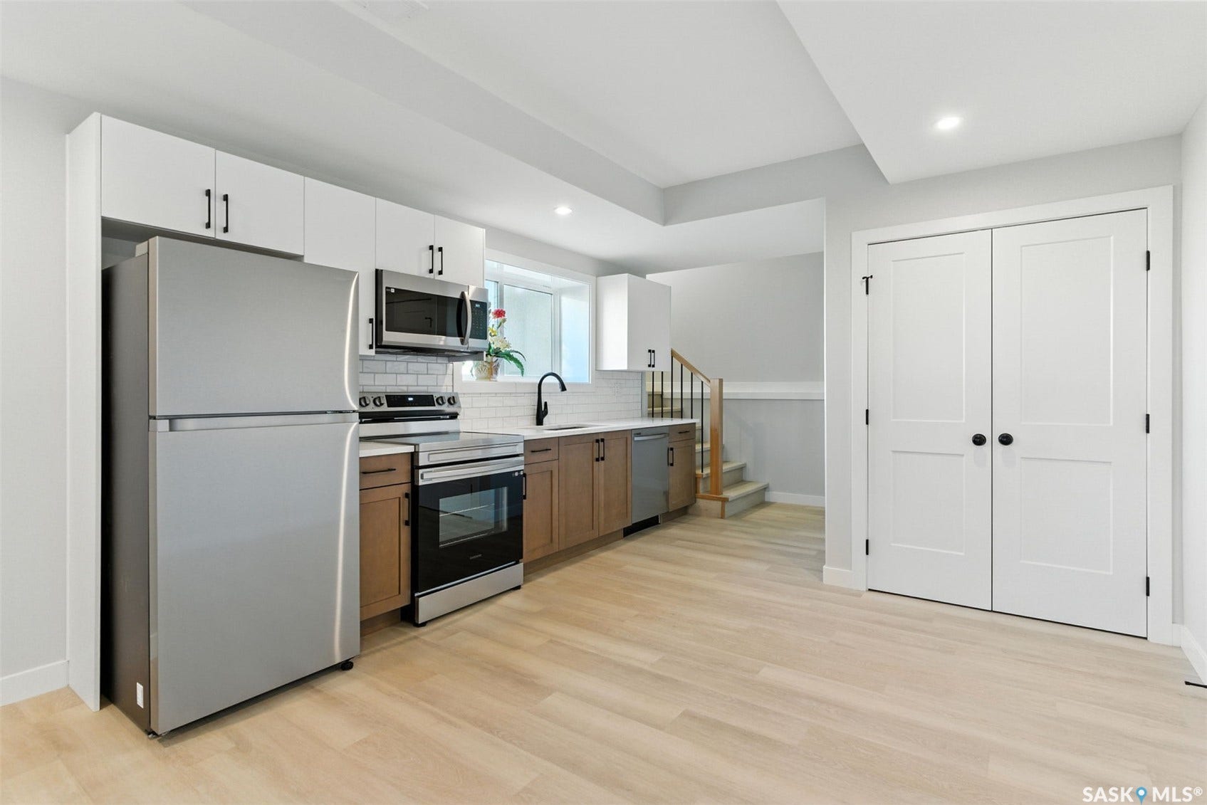Kitchen featuring stainless steel appliances, white shaker-style upper cabinetry, wood-finish lower cabinetry, and light wood-finish flooring