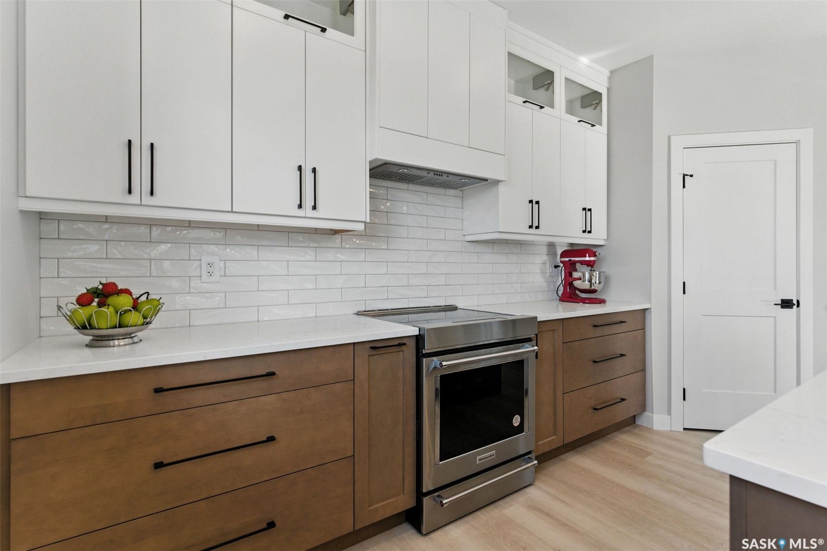Stainless steel range with a built-in oven, solid surface countertops, white subway tile backsplash, two-tone cabinetry with contrasting hardware, and wood-finish flooring