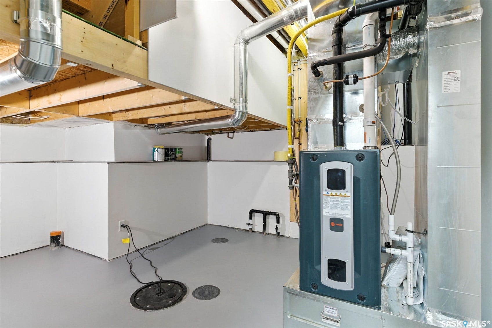 Unfinished basement space featuring exposed joists, a furnace, and a sump pump