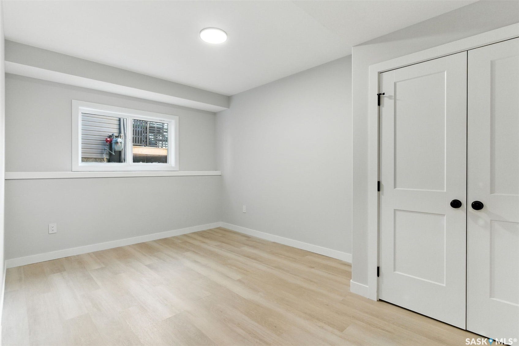 Recessed ceiling lighting, wood-finish flooring, white trim, white paneled doors with matte black hardware, and a single window