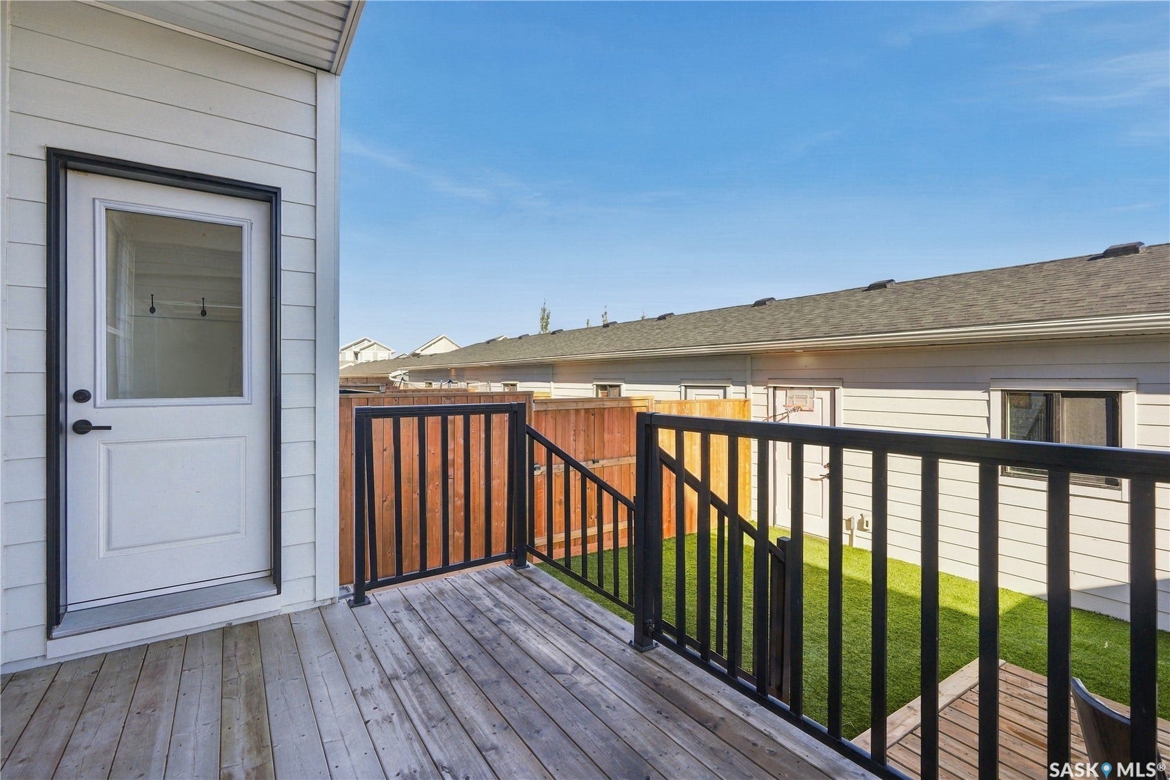 Outdoor wooden deck with black metal railings, white exterior siding, and a back door with a window