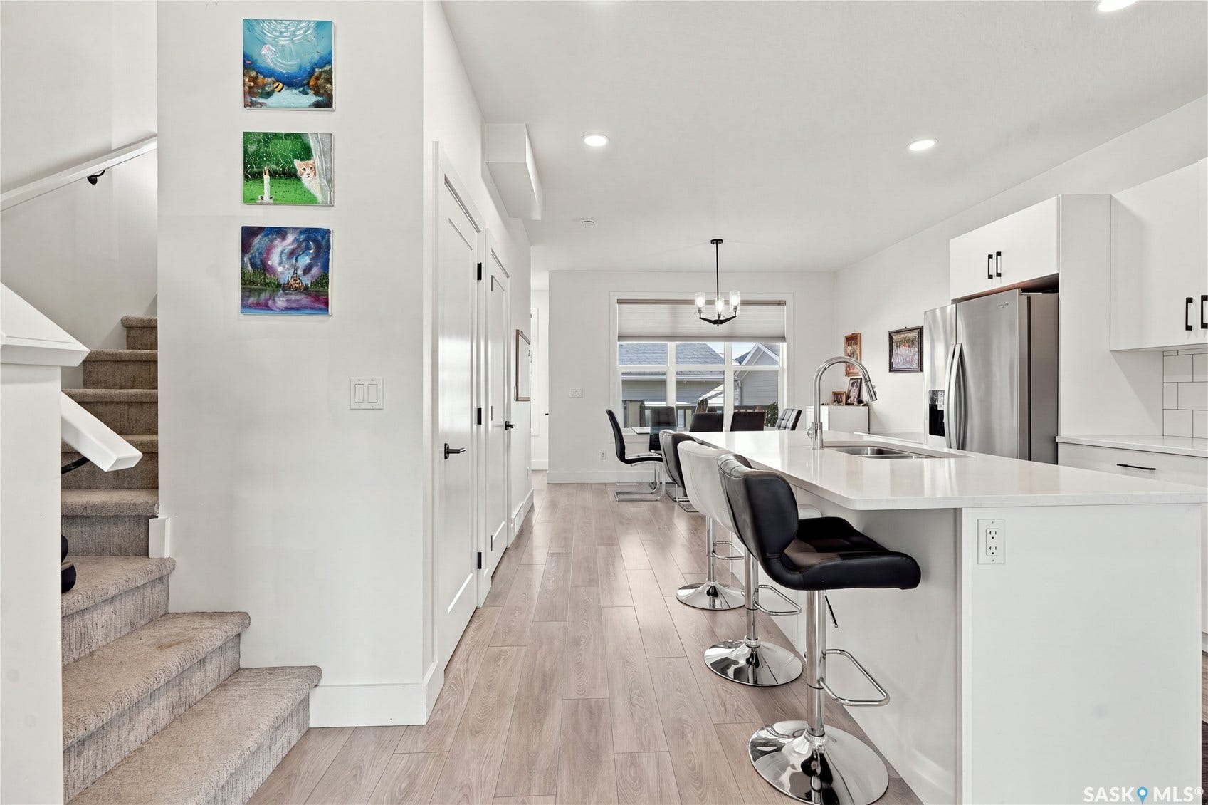 Open-concept living space with light wood-finish flooring, white kitchen cabinetry, a kitchen island with seating, a stainless steel refrigerator, and recessed lighting