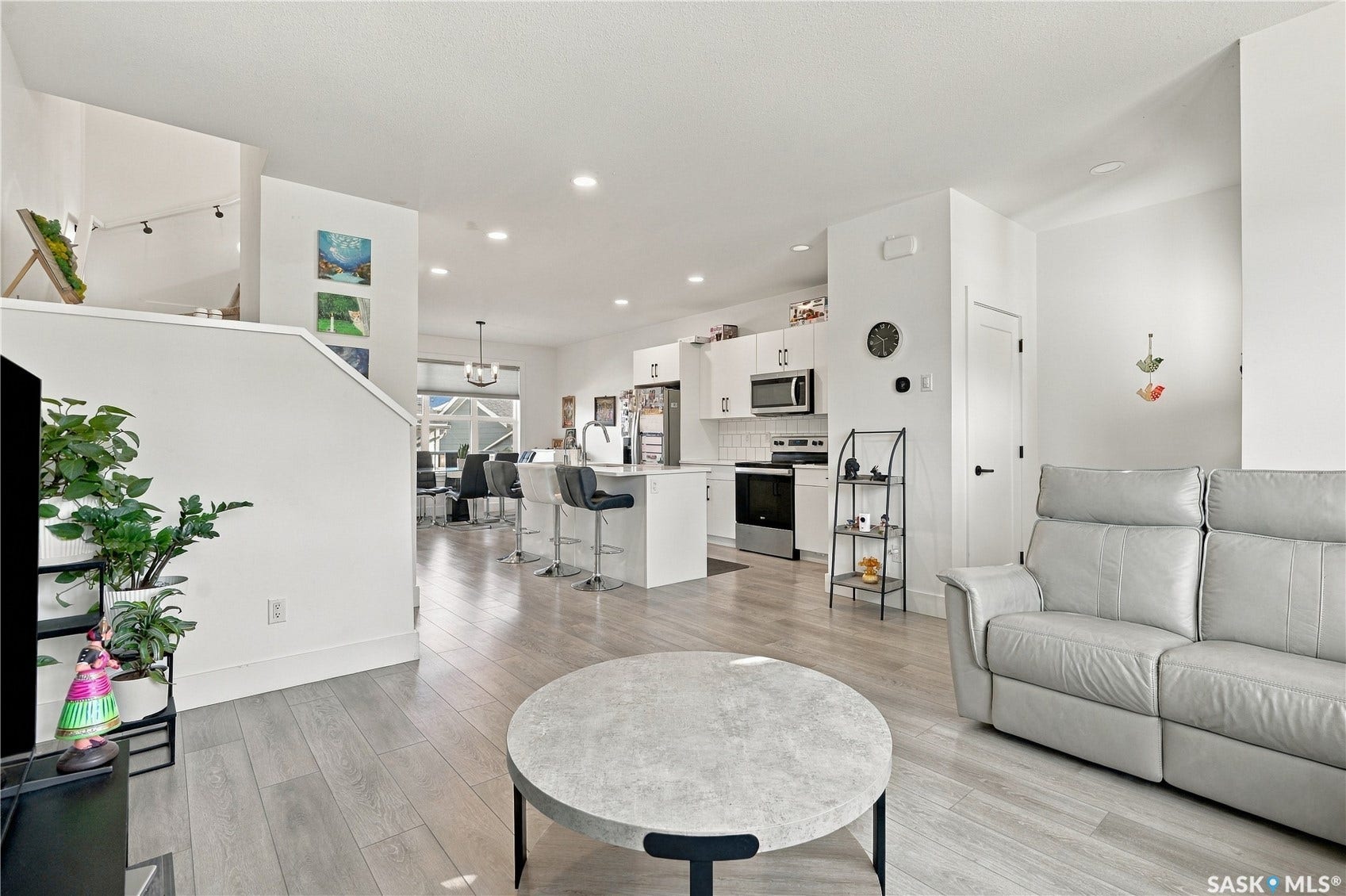 Open-concept living area with light wood-finish flooring, white walls, recessed lighting, and a kitchen featuring white cabinetry and stainless steel appliances