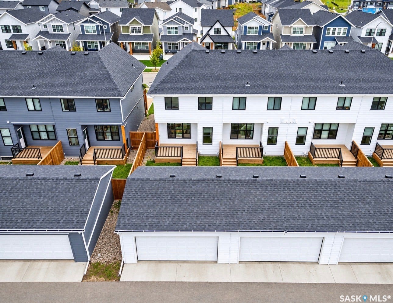 Modern townhome exteriors featuring multiple windows, private rear decks with wood railings, and detached garages with white doors