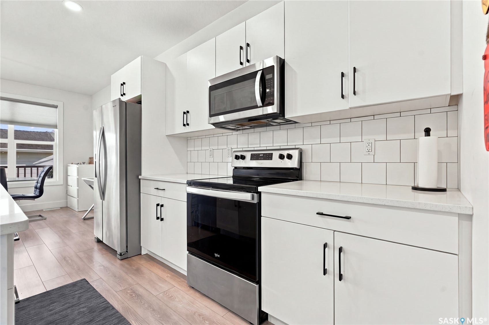 White cabinetry with dark hardware, stainless steel appliances, white subway tile backsplash, light-toned countertops, and wood-finish flooring