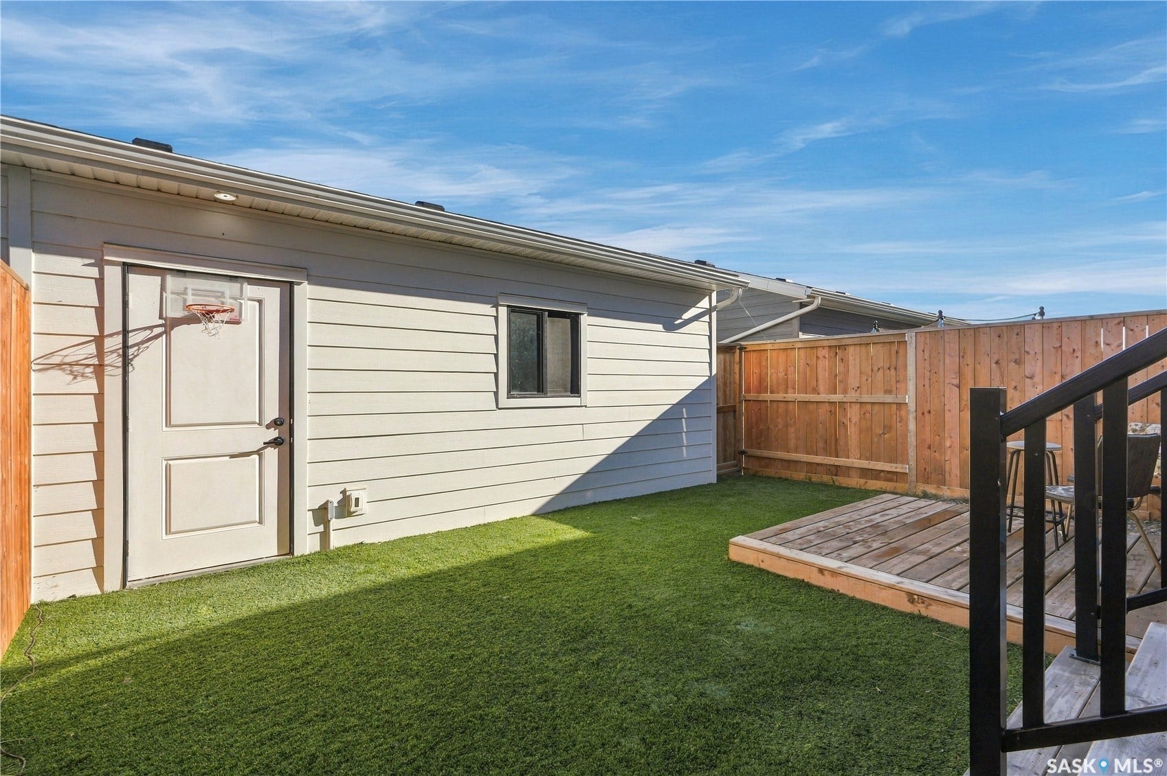 Manicured artificial turf lawn, elevated wooden deck, wood privacy fencing, and exterior wall with window