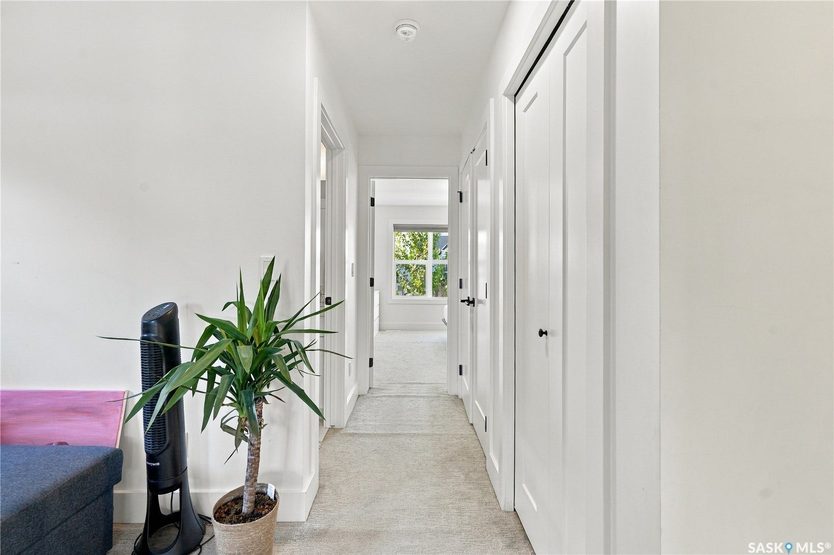 Hallway featuring light-toned carpeting, white walls, and white doors with dark hardware