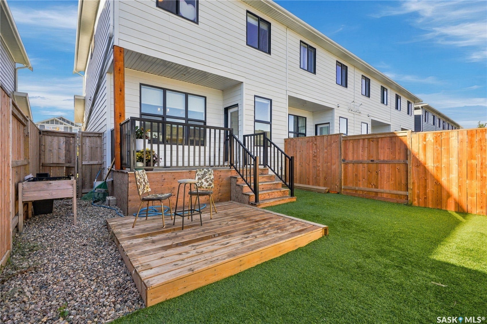 Rear exterior featuring a wood deck, artificial turf, and privacy fencing