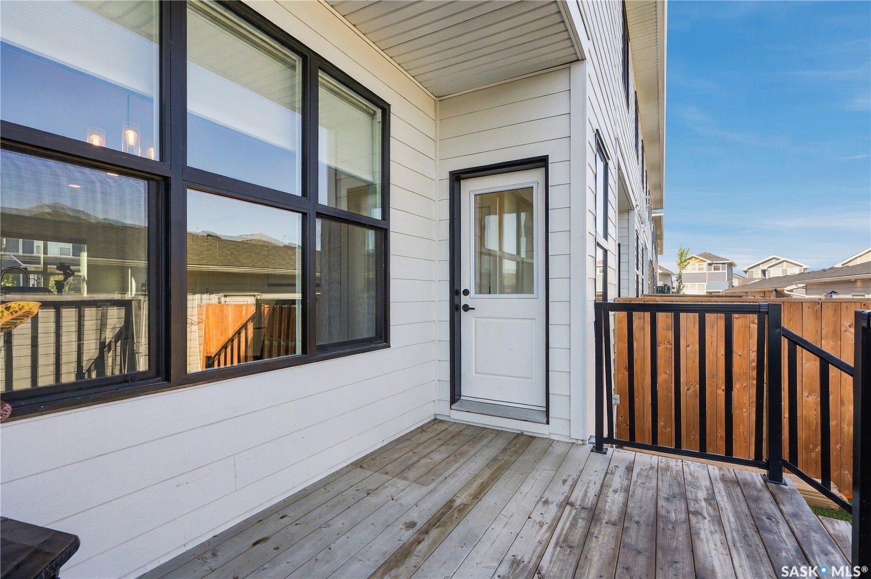 Exterior deck with wood-finish flooring, white siding, black-framed windows, and a white exterior door
