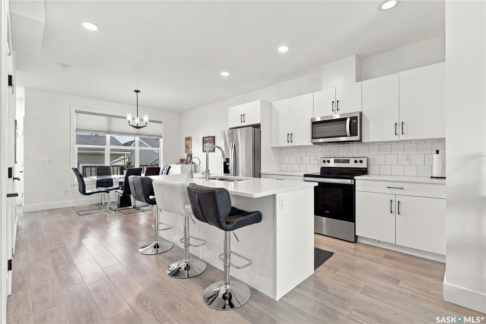 White kitchen cabinetry with stainless steel appliances, white subway tile backsplash, and light wood-finish flooring
