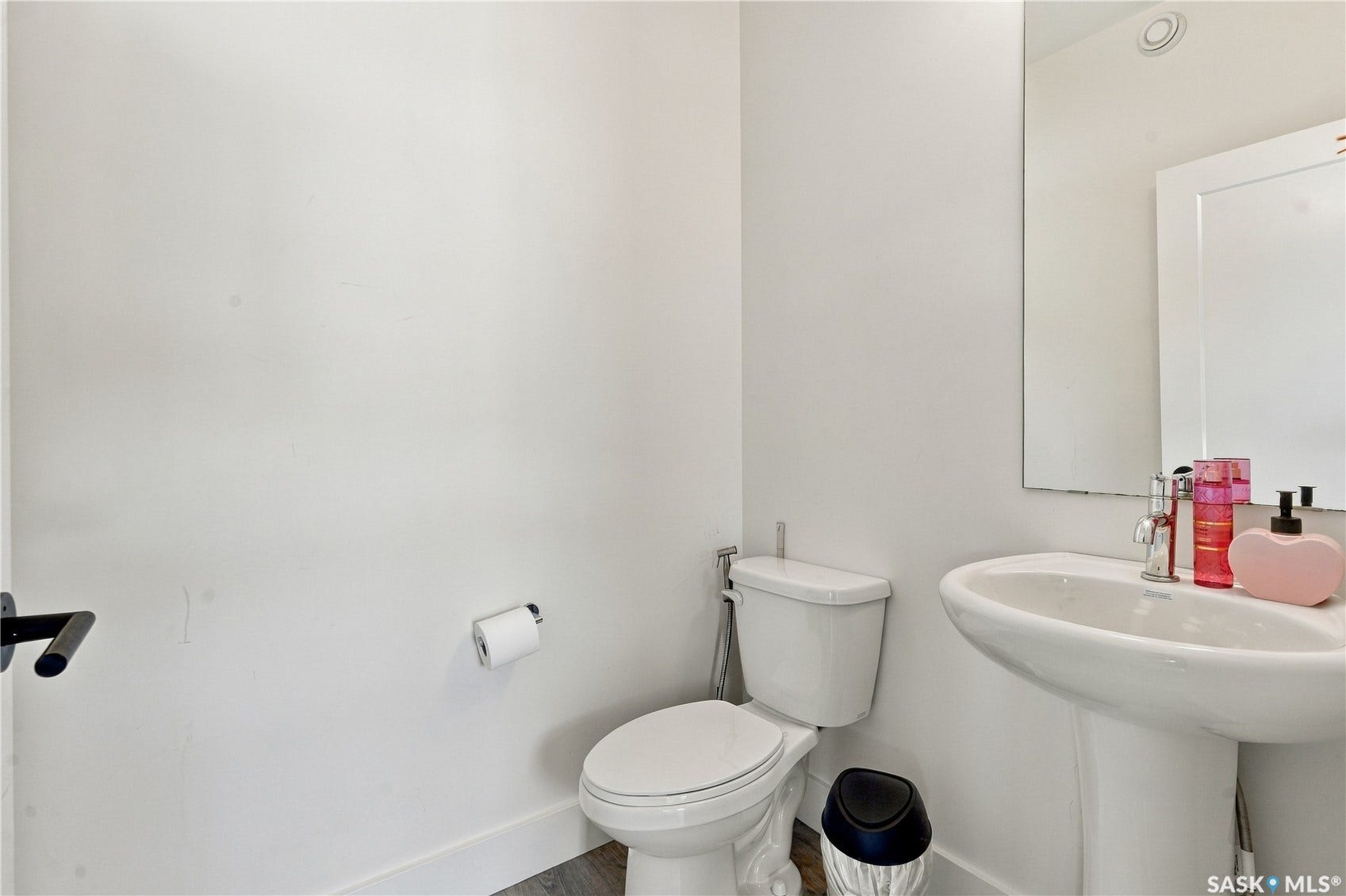 Pedestal sink with chrome faucet, wall-mounted mirror, and wood-finish flooring